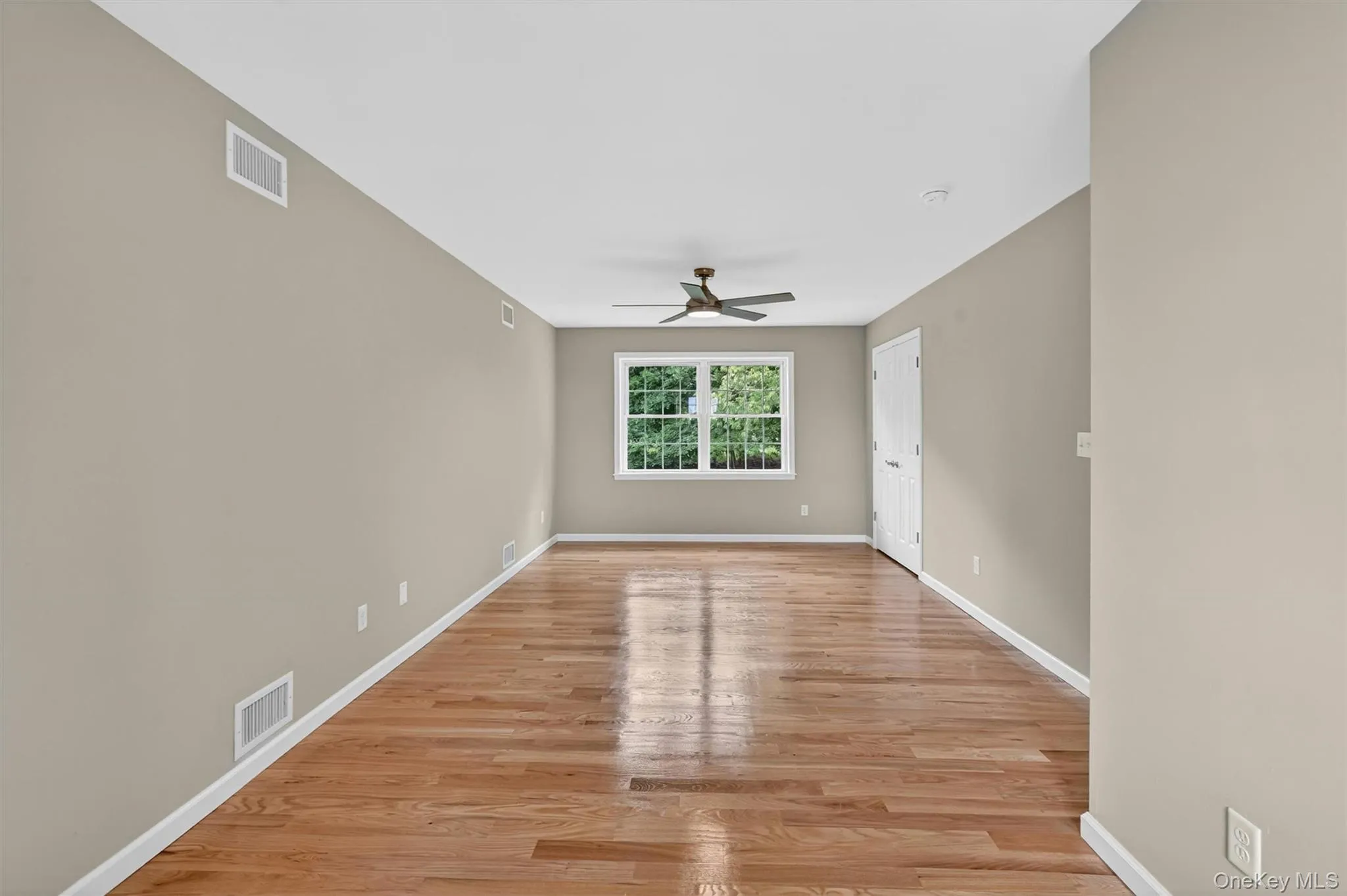Spacious room featuring wood-finish flooring, a ceiling fan, and a large window with white trim Spacious room featuring wood-finish flooring, a ceiling fan, and a large window with white trim