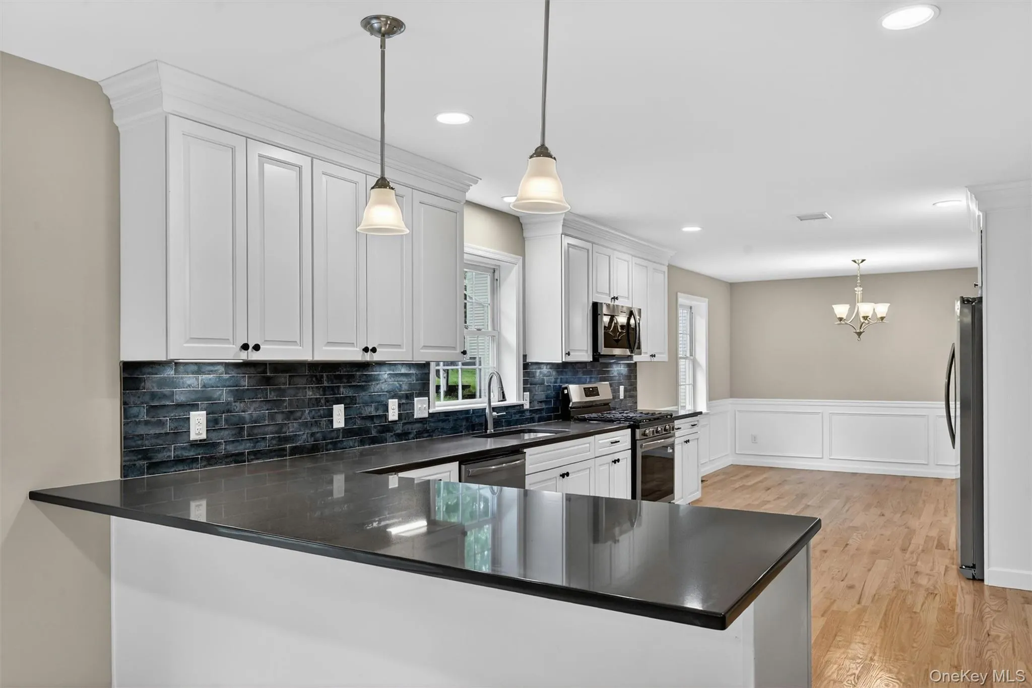 Modern kitchen featuring white shaker cabinetry, dark countertops, a dark tile backsplash, and stainless steel appliances Modern kitchen featuring white shaker cabinetry, dark countertops, a dark tile backsplash, and stainless steel appliances