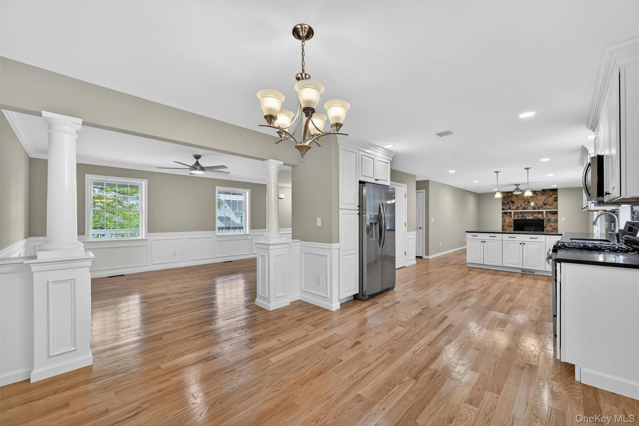 Open-concept kitchen featuring white cabinetry, stainless steel appliances, dark countertops, and wood-finish flooring Open-concept kitchen featuring white cabinetry, stainless steel appliances, dark countertops, and wood-finish flooring