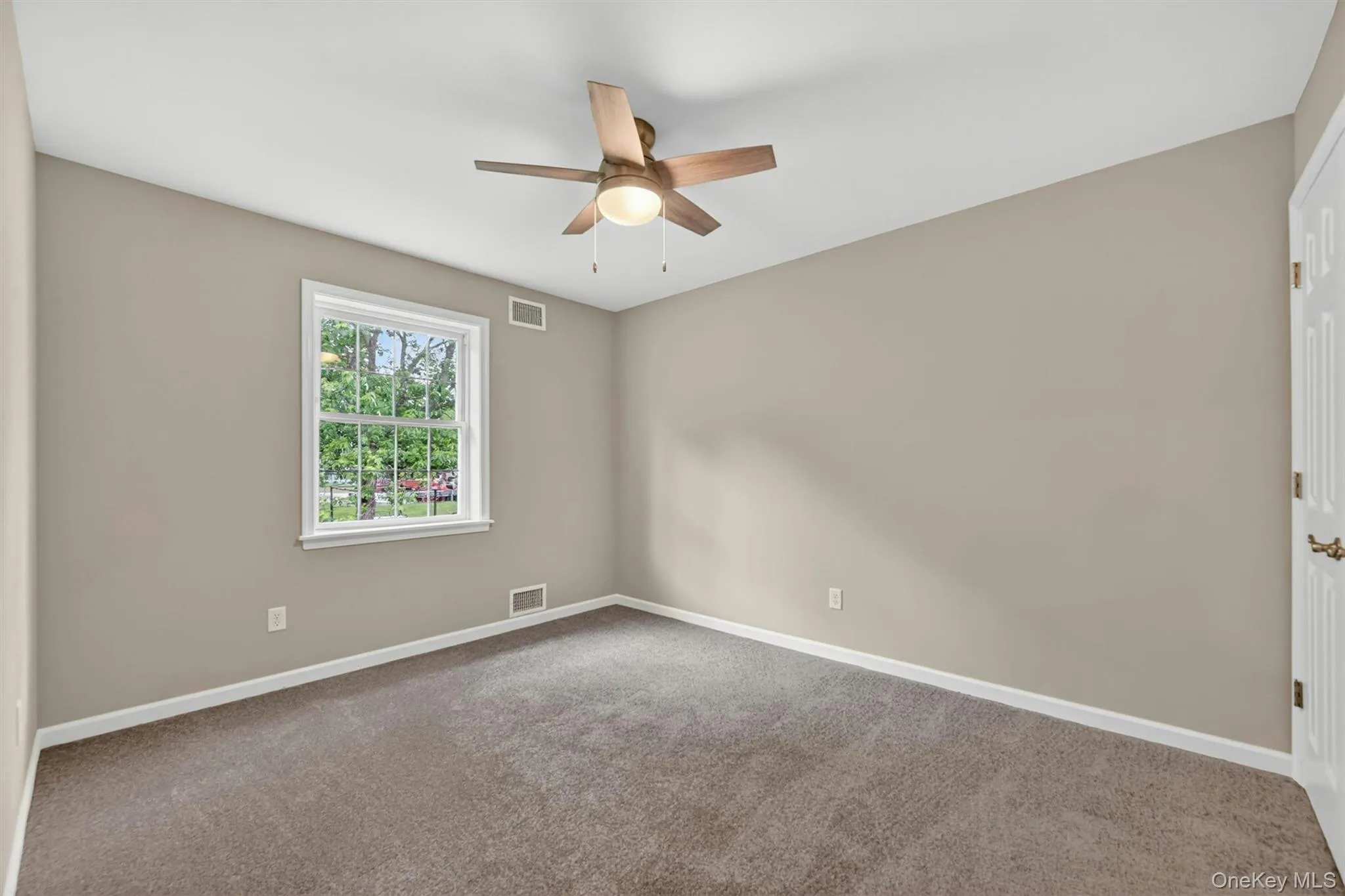 Neutral-toned room featuring a ceiling fan with light fixture, carpeted flooring, and a white-framed window Neutral-toned room featuring a ceiling fan with light fixture, carpeted flooring, and a white-framed window