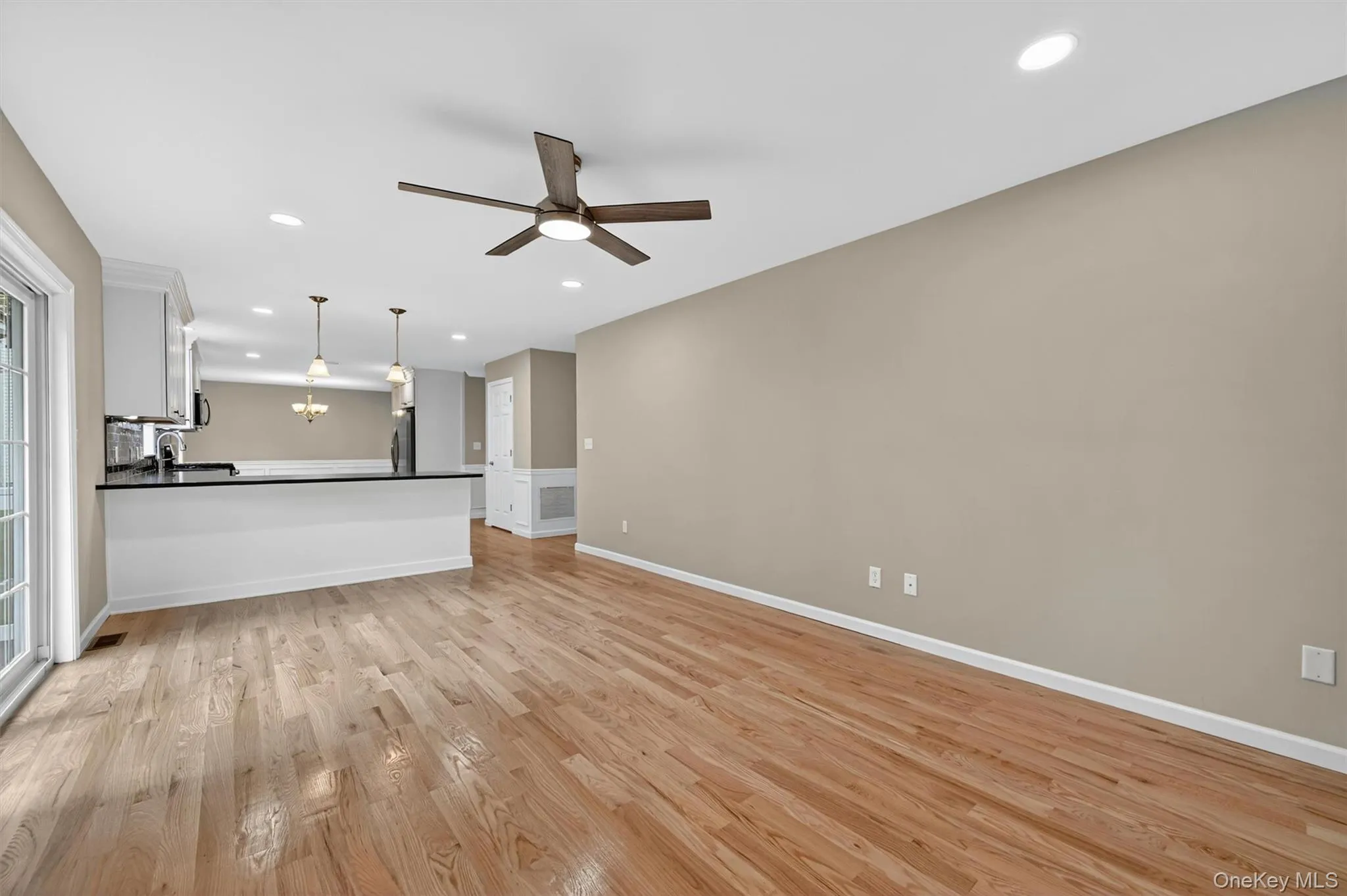 Expansive living area with wood-finish flooring, recessed lighting, and a ceiling fan Expansive living area with wood-finish flooring, recessed lighting, and a ceiling fan
