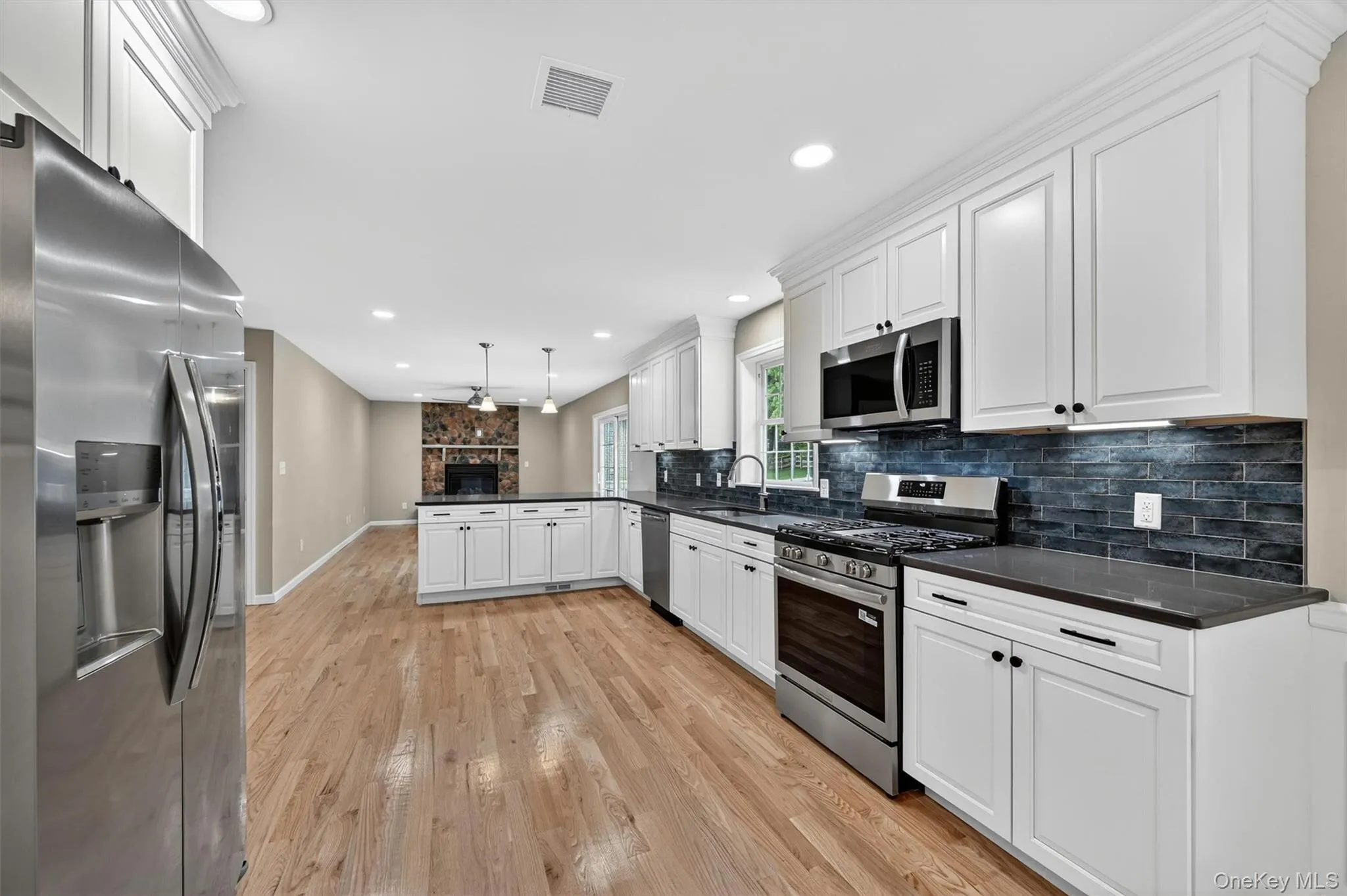 Open-concept kitchen featuring white cabinetry, stainless steel appliances, dark countertops, and wood-finish flooring Open-concept kitchen featuring white cabinetry, stainless steel appliances, dark countertops, and wood-finish flooring