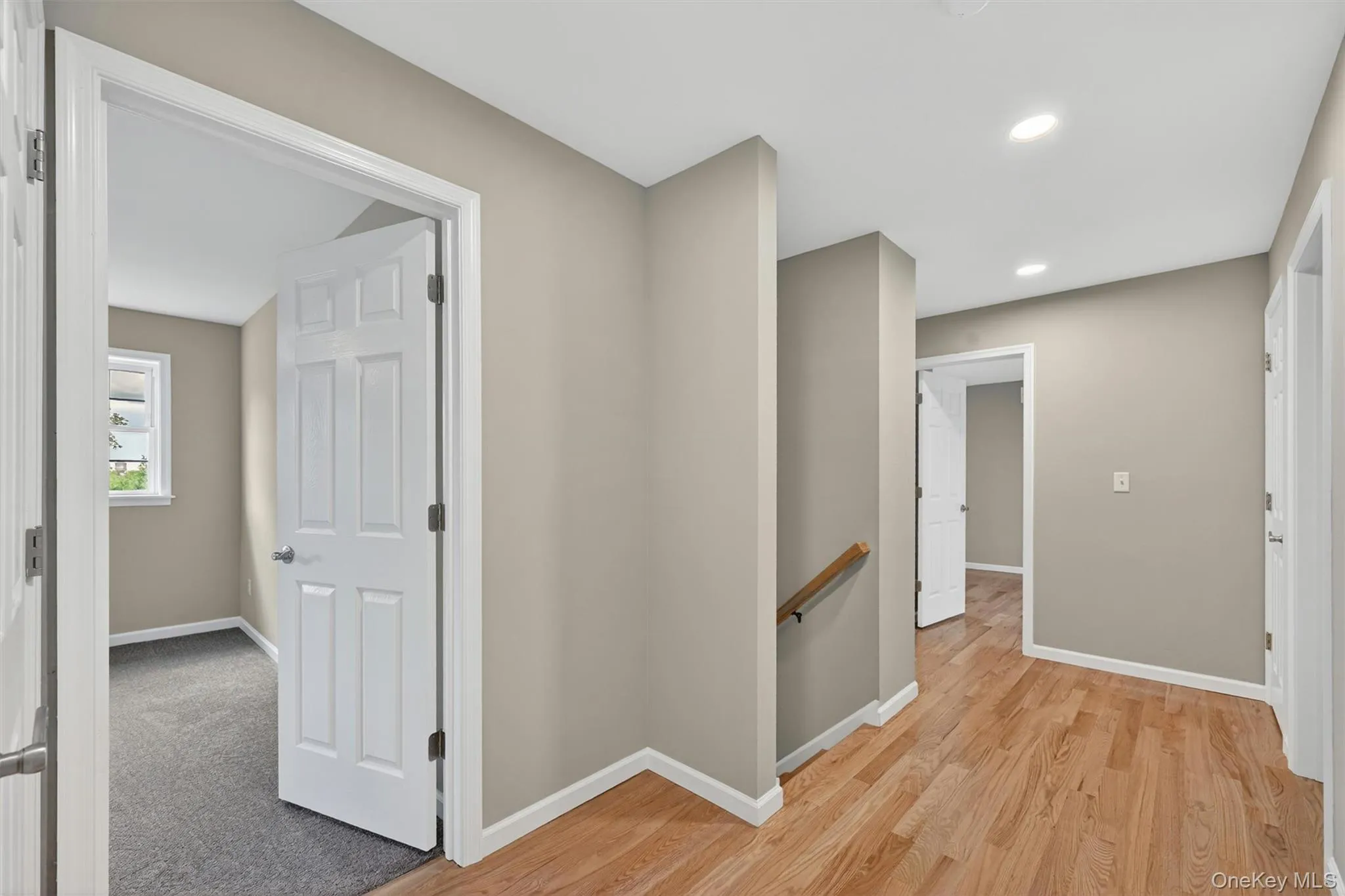 Hallway with wood-finish flooring, light tan walls, and white trim Hallway with wood-finish flooring, light tan walls, and white trim