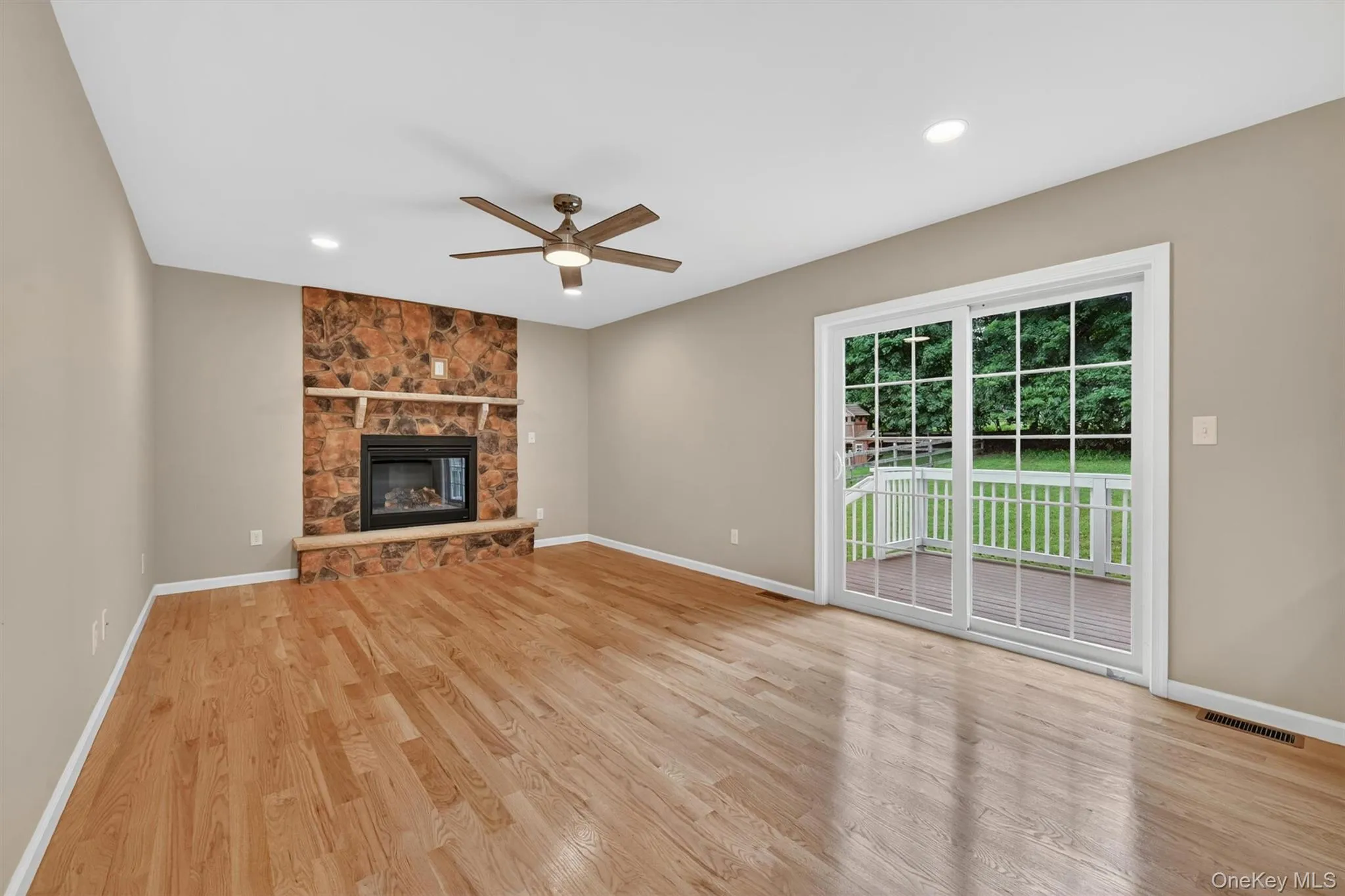 Living area featuring hardwood flooring, a stone-faced fireplace with hearth and mantel, recessed lighting, and a ceiling fan Living area featuring hardwood flooring, a stone-faced fireplace with hearth and mantel, recessed lighting, and a ceiling fan