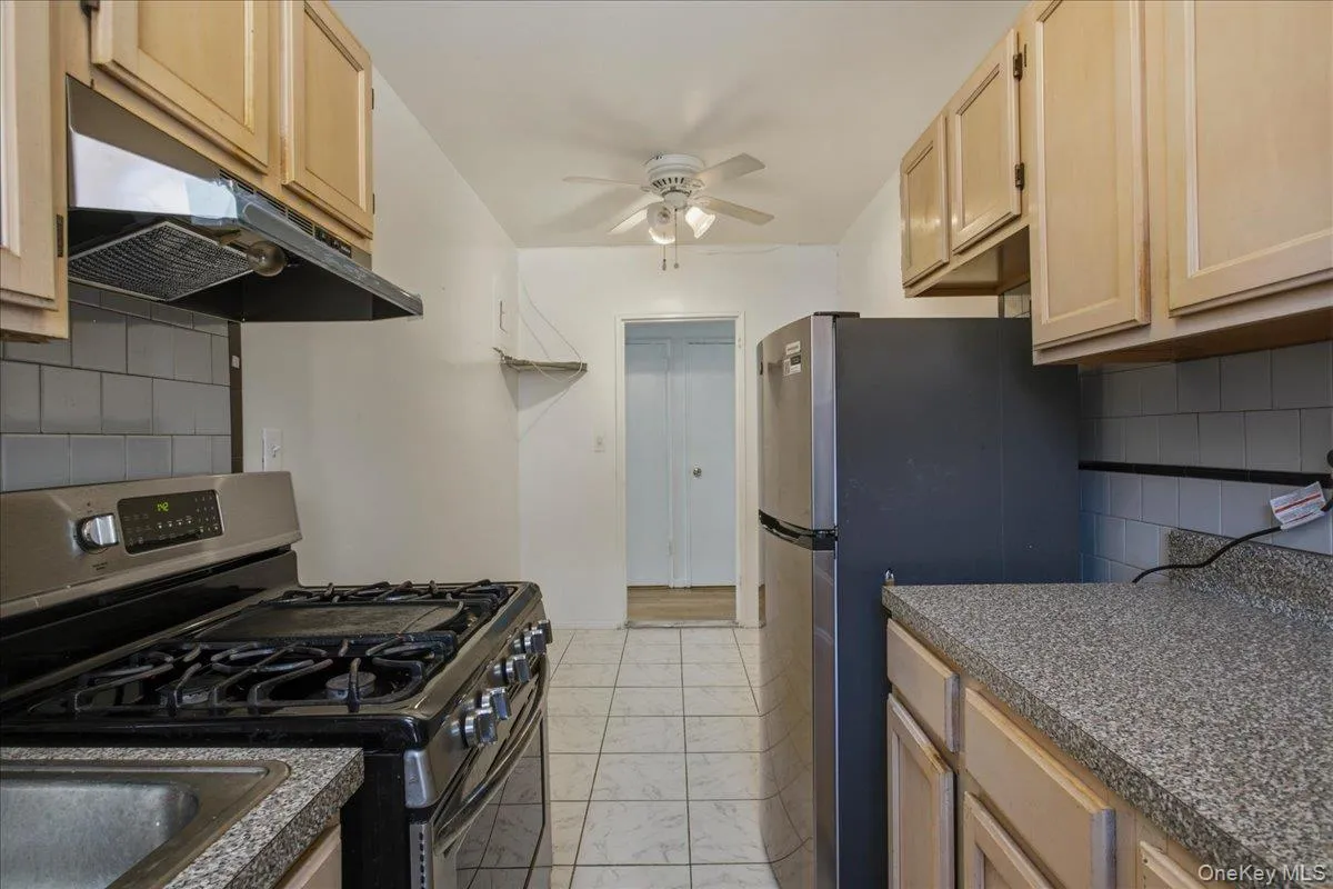 Kitchen view from far end by window. light wood cabinetry w complimentary speckled counters and a stainless sink. Kitchen view from far end by window. light wood cabinetry w complimentary speckled counters and a stainless sink.