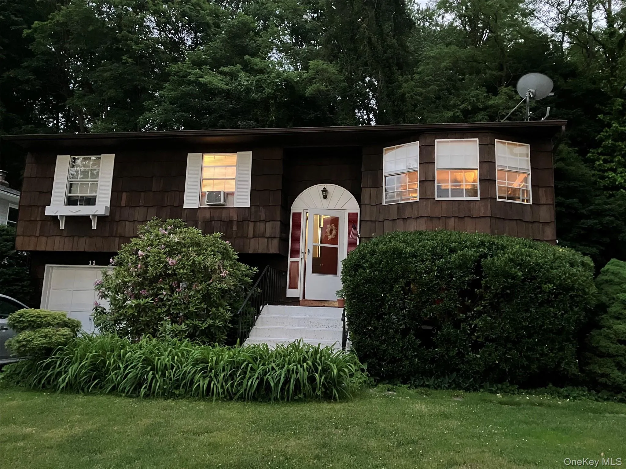 Evening View of residence featuring a shake shingle exterior, an arched entry, and white window shutters Evening View of residence featuring a shake shingle exterior, an arched entry, and white window shutters
