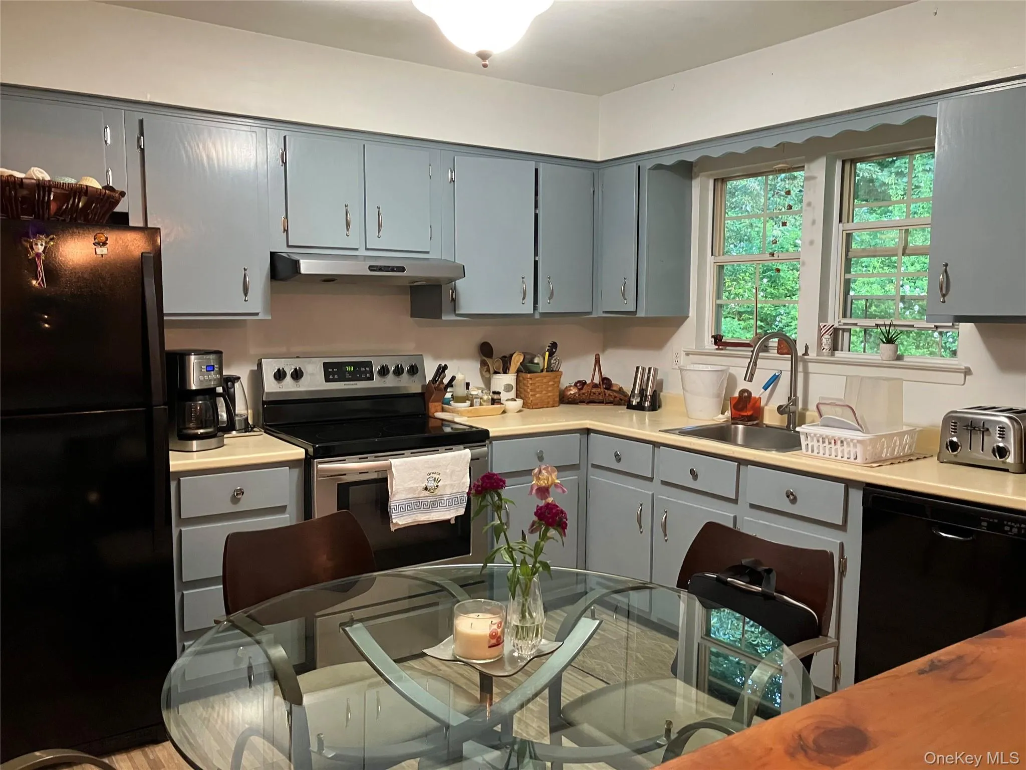 Eat-In-Kitchen featuring light blue cabinetry, light-toned countertops, a stainless steel electric range with an overhead vent, and a double window above the sink Eat-In-Kitchen featuring light blue cabinetry, light-toned countertops, a stainless steel electric range with an overhead vent, and a double window above the sink