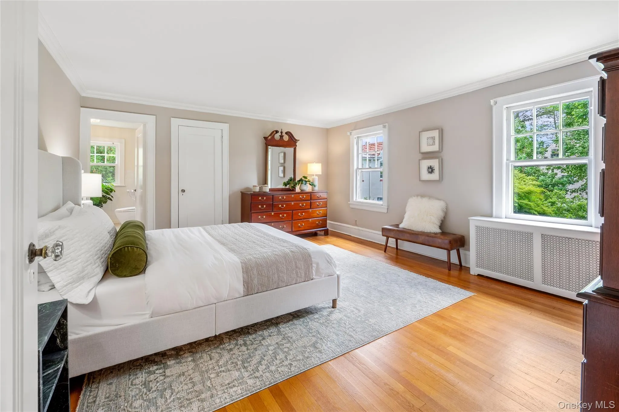 Spacious bedroom featuring hardwood flooring, light neutral wall paint, and white crown molding Spacious bedroom featuring hardwood flooring, light neutral wall paint, and white crown molding
