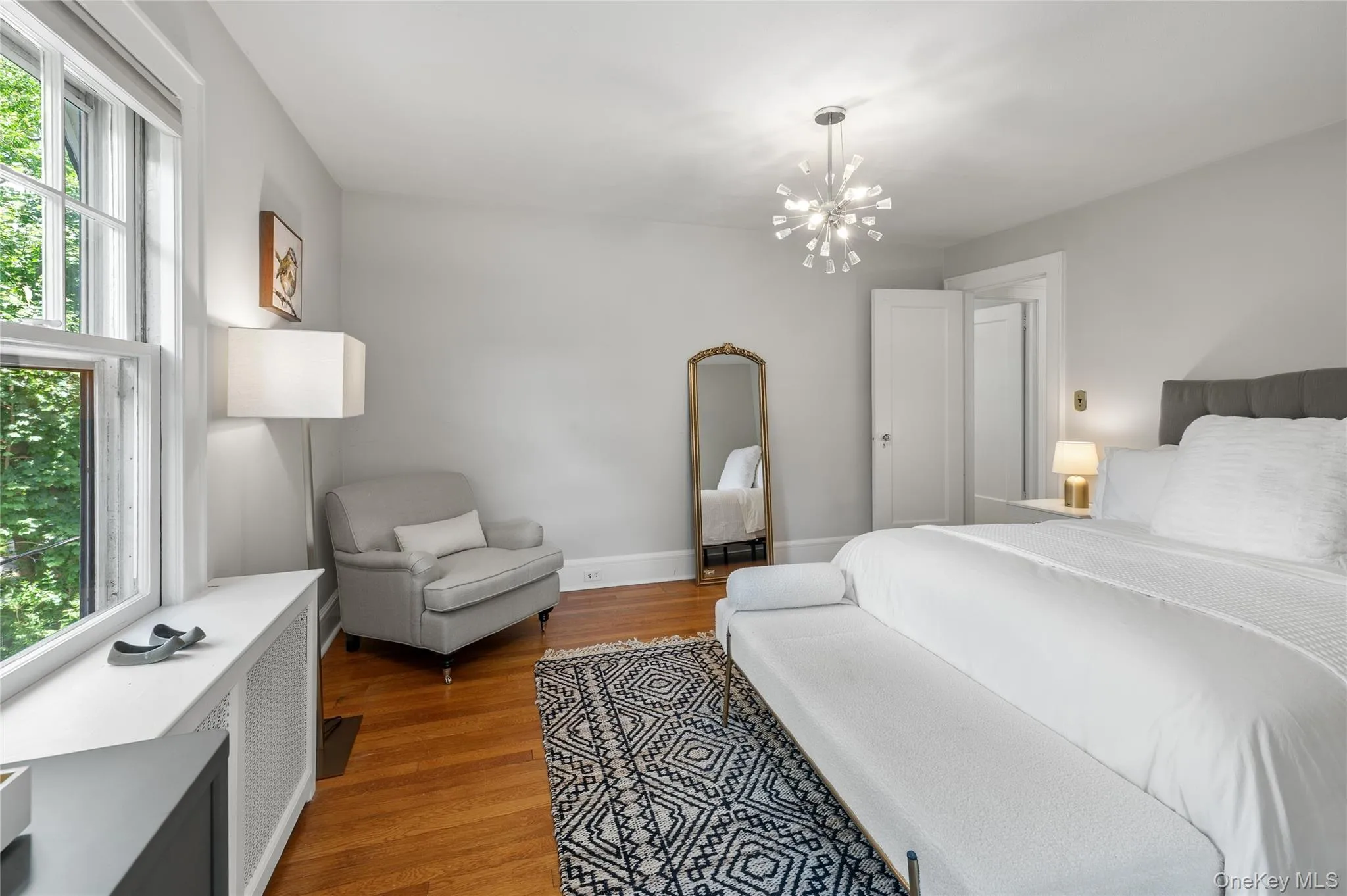 Bright room featuring hardwood flooring, a contemporary chandelier, large window, and light gray wall tones Bright room featuring hardwood flooring, a contemporary chandelier, large window, and light gray wall tones