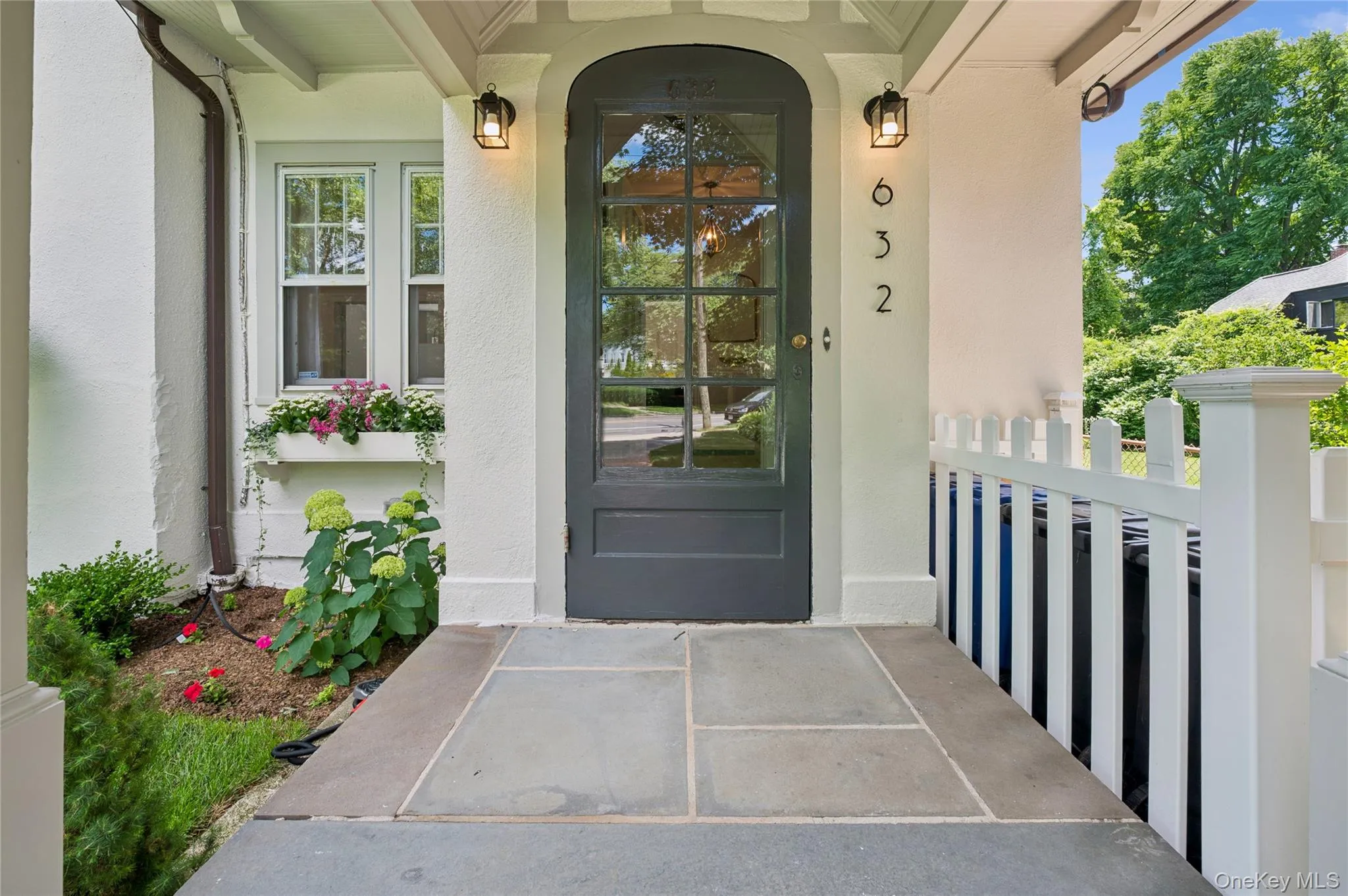 Arched entry door with glass panels, flanked by exterior wall sconces, above a flagstone entry patio Arched entry door with glass panels, flanked by exterior wall sconces, above a flagstone entry patio