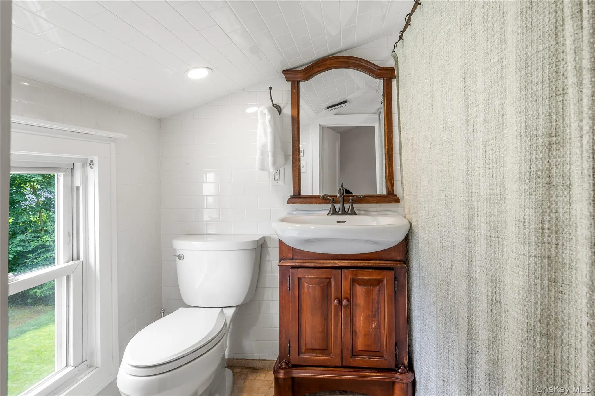 Bathroom featuring a white toilet, wood-finish vanity with an integrated sink, and an arched mirror Bathroom featuring a white toilet, wood-finish vanity with an integrated sink, and an arched mirror