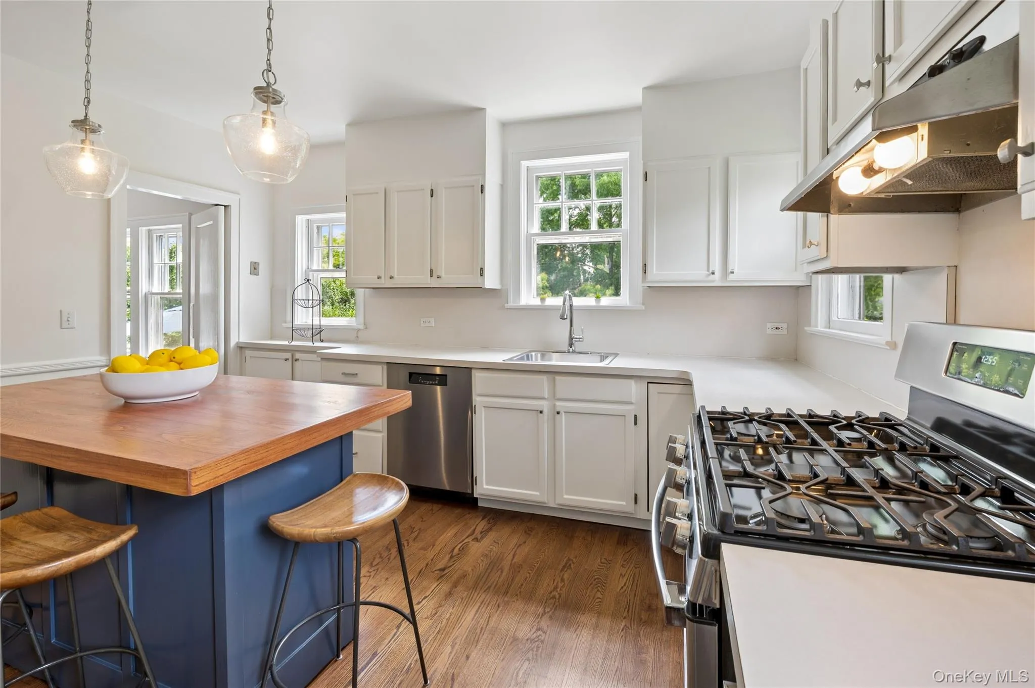 Kitchen featuring an island with a wood-finish countertop, white cabinetry, light-toned countertops, a stainless steel gas range, and wood-finish flooring Kitchen featuring an island with a wood-finish countertop, white cabinetry, light-toned countertops, a stainless steel gas range, and wood-finish flooring