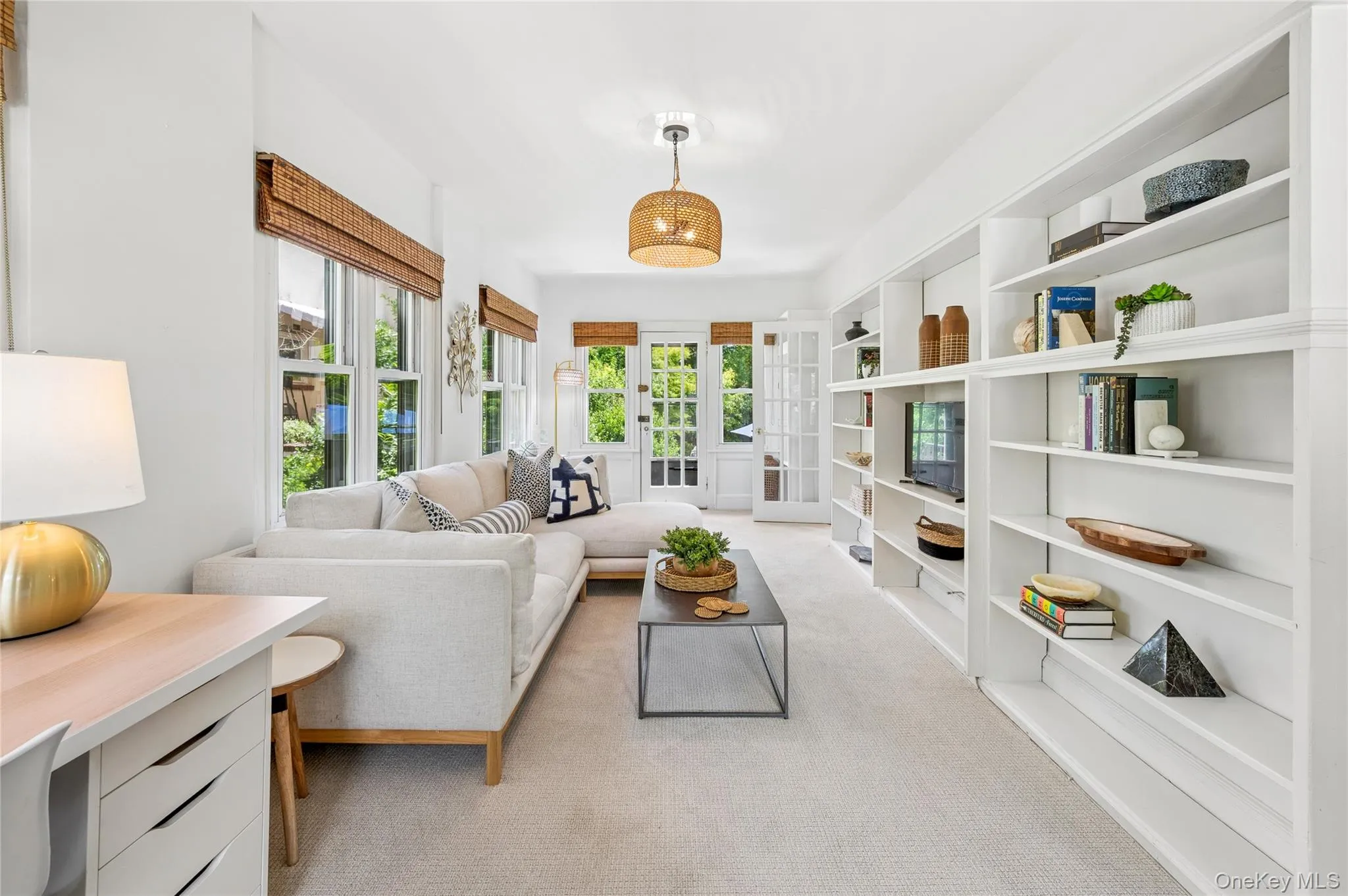 Expansive family room featuring extensive built-in shelving, multiple large windows with natural light, and double French doors opening to outdoor areas Expansive family room featuring extensive built-in shelving, multiple large windows with natural light, and double French doors opening to outdoor areas