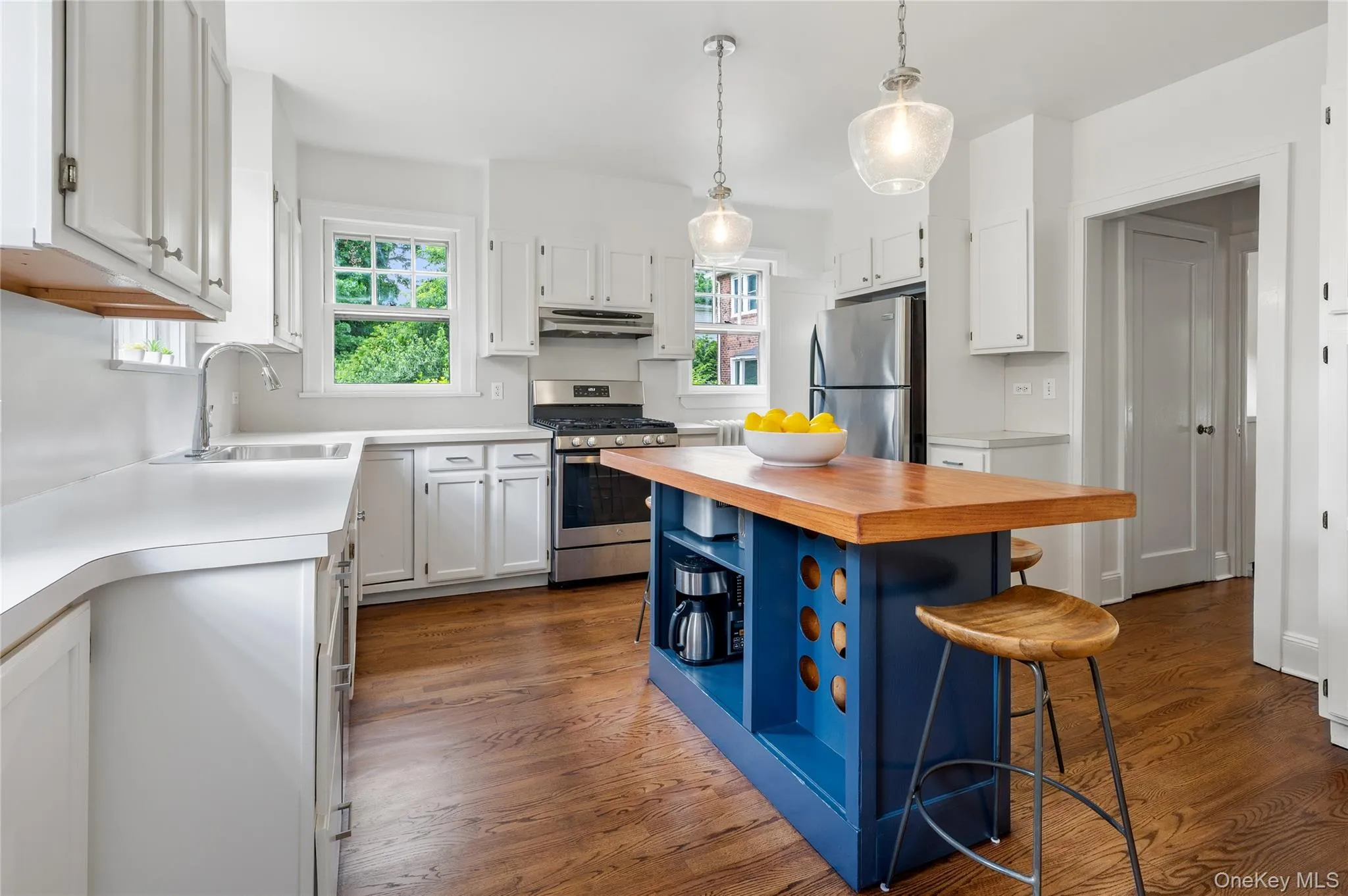Kitchen featuring a blue-painted island with a wood-finish countertop, white cabinetry, stainless steel appliances, white countertops, and wood-finish flooring Kitchen featuring a blue-painted island with a wood-finish countertop, white cabinetry, stainless steel appliances, white countertops, and wood-finish flooring