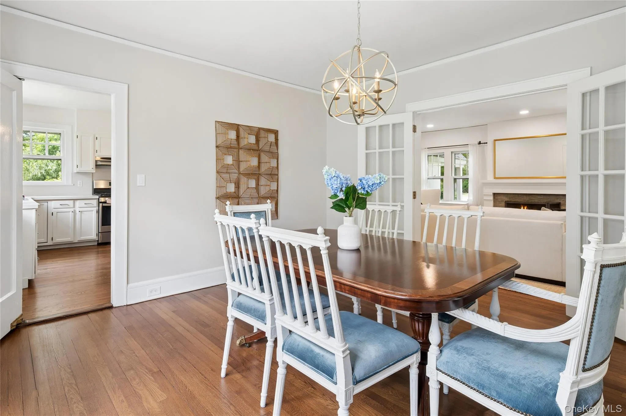 Dining area featuring wood-finish flooring, a contemporary spherical chandelier, and double French doors opening into a living space Dining area featuring wood-finish flooring, a contemporary spherical chandelier, and double French doors opening into a living space