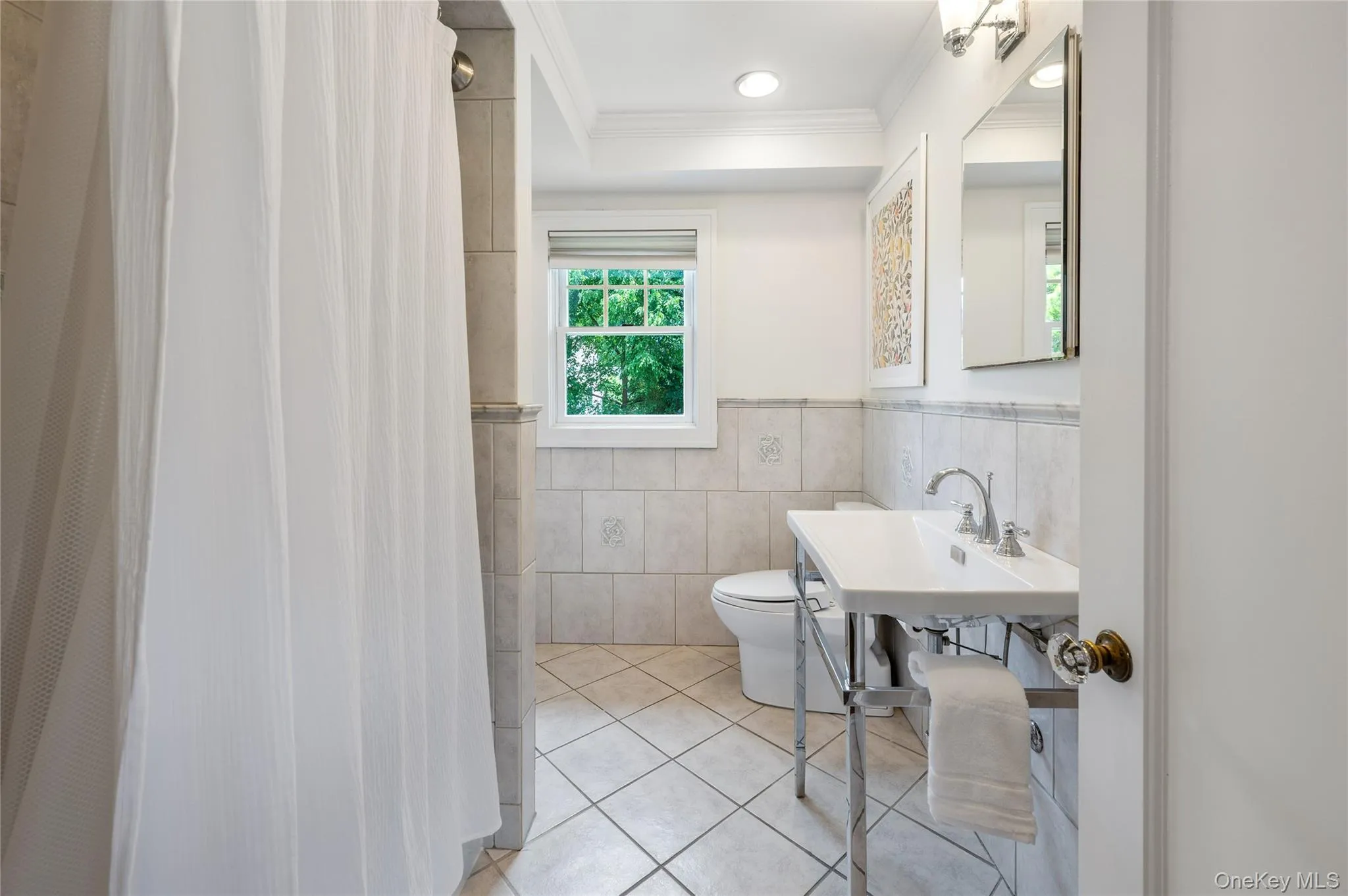 Bathroom featuring floor-to-ceiling tile, a pedestal sink with chrome fixtures, a window with natural light, and crown molding Bathroom featuring floor-to-ceiling tile, a pedestal sink with chrome fixtures, a window with natural light, and crown molding