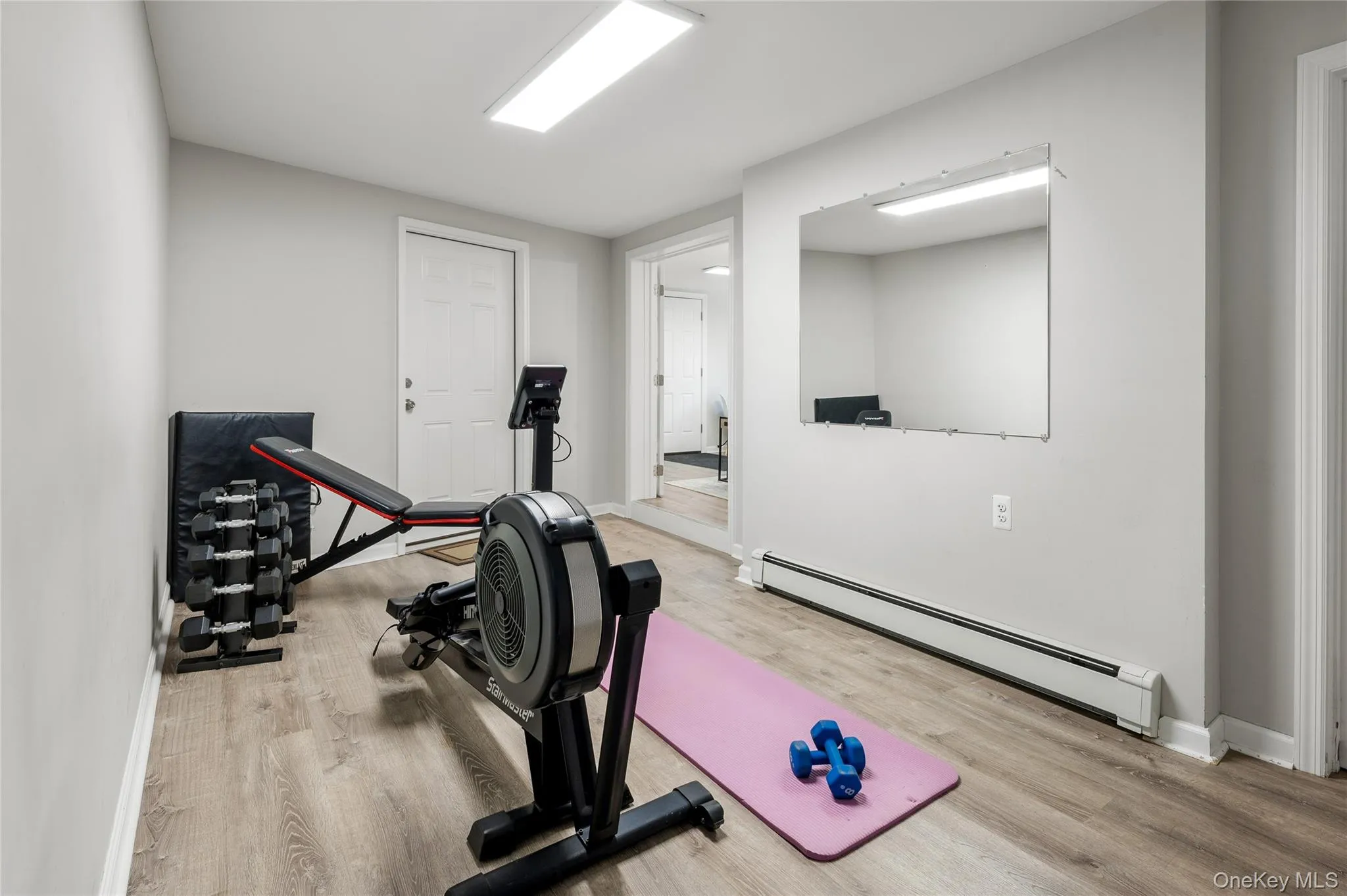 Versatile room featuring wood-finish flooring, light grey walls, and a large wall-mounted mirror Versatile room featuring wood-finish flooring, light grey walls, and a large wall-mounted mirror