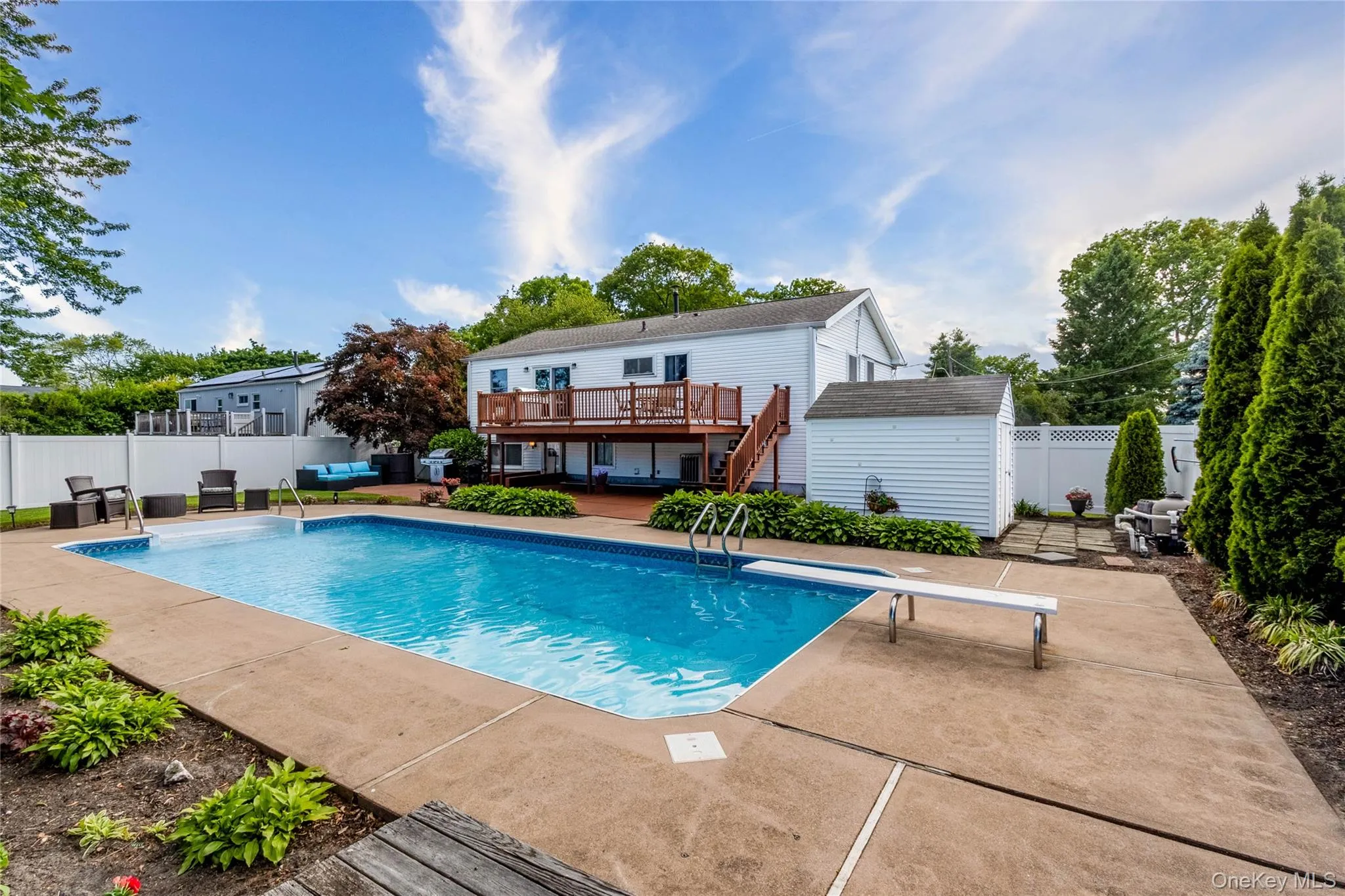 Expansive backyard featuring a large in-ground swimming pool with a diving board, surrounded by a concrete patio Expansive backyard featuring a large in-ground swimming pool with a diving board, surrounded by a concrete patio