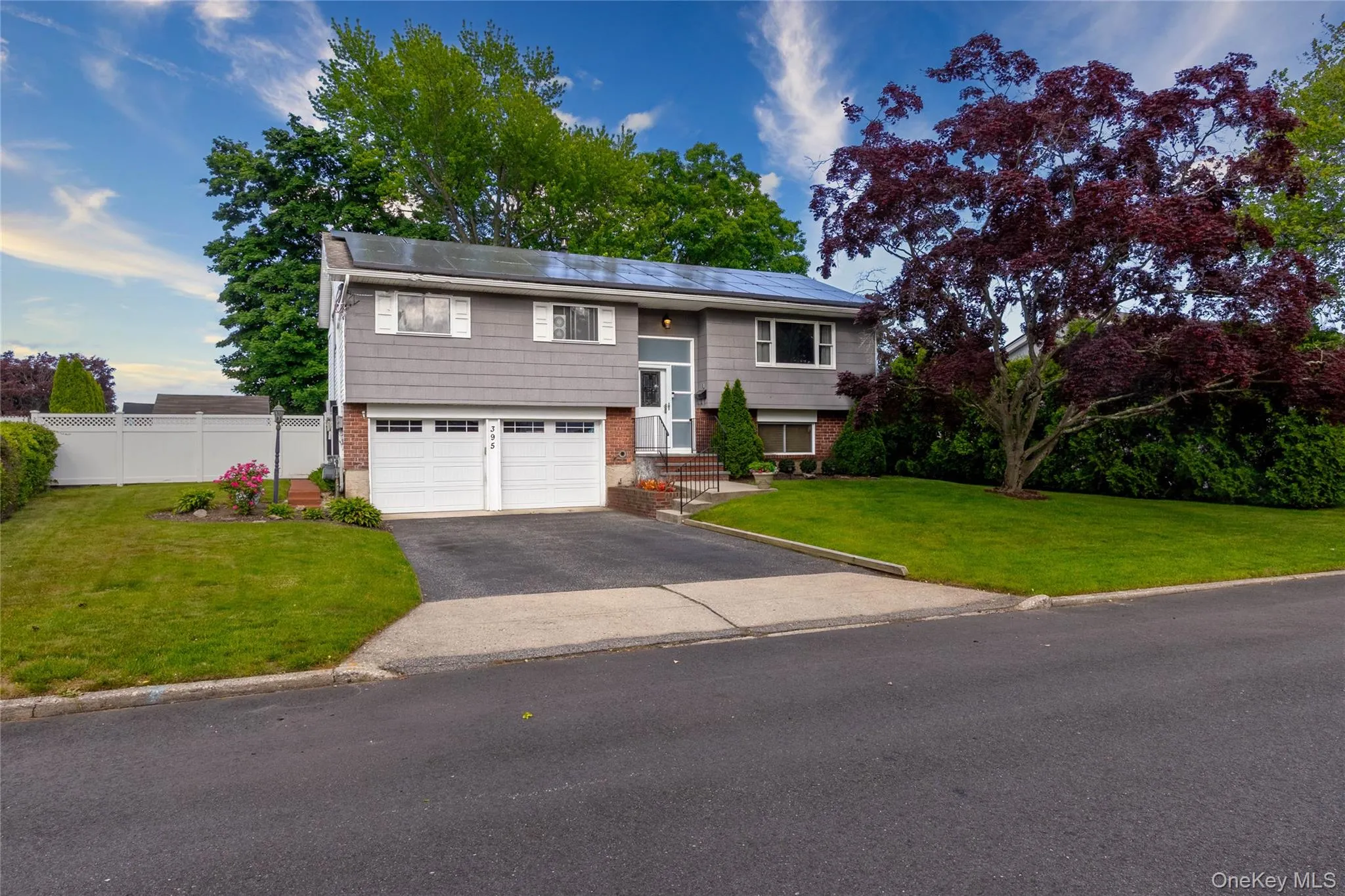 Split-level residence featuring gray siding, a two-car garage, and a paved driveway Split-level residence featuring gray siding, a two-car garage, and a paved driveway