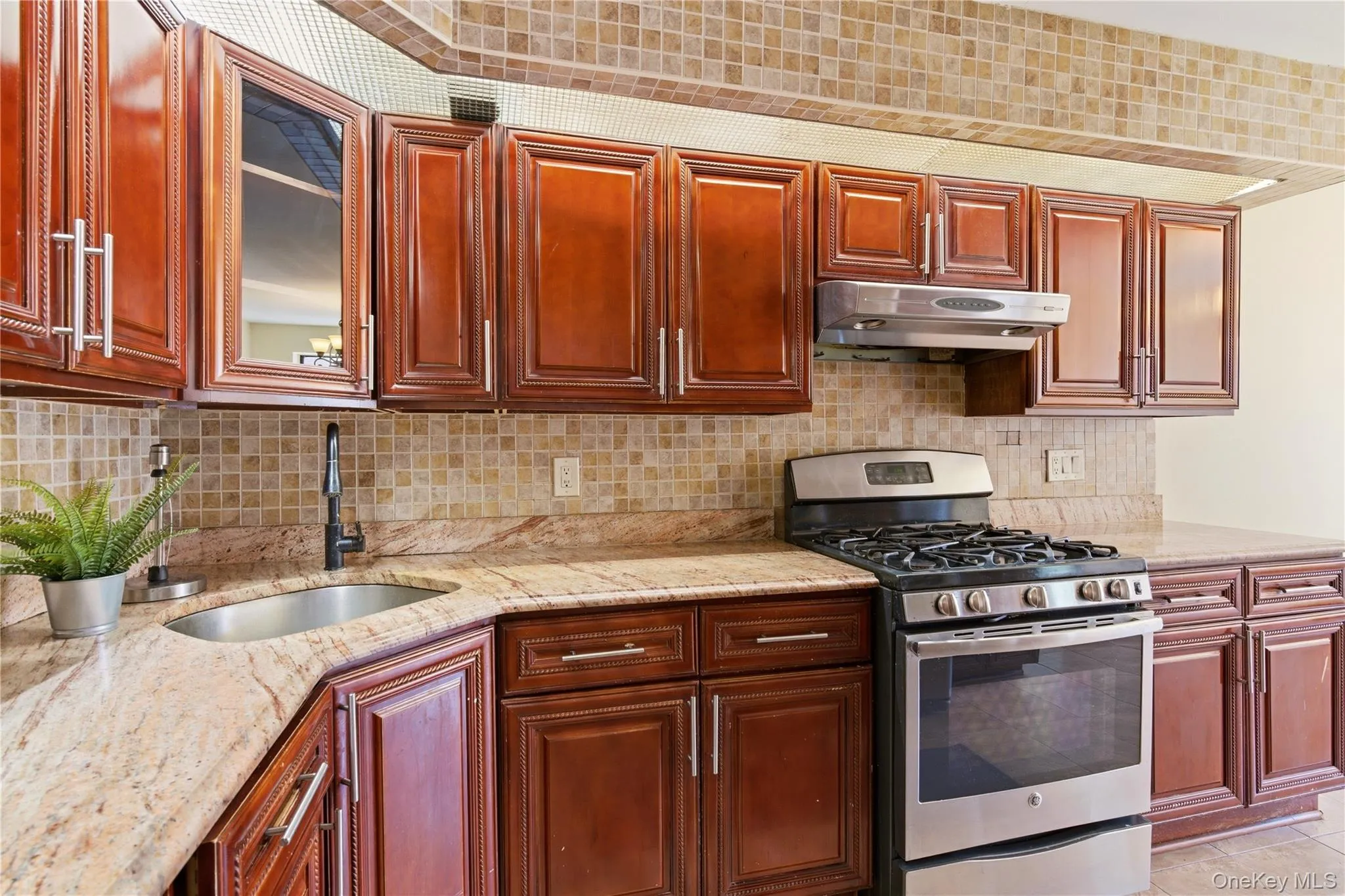 Kitchen with rich wood cabinetry, stainless steel appliances, a corner sink with a black faucet, and patterned mosaic tile backsplash Kitchen with rich wood cabinetry, stainless steel appliances, a corner sink with a black faucet, and patterned mosaic tile backsplash
