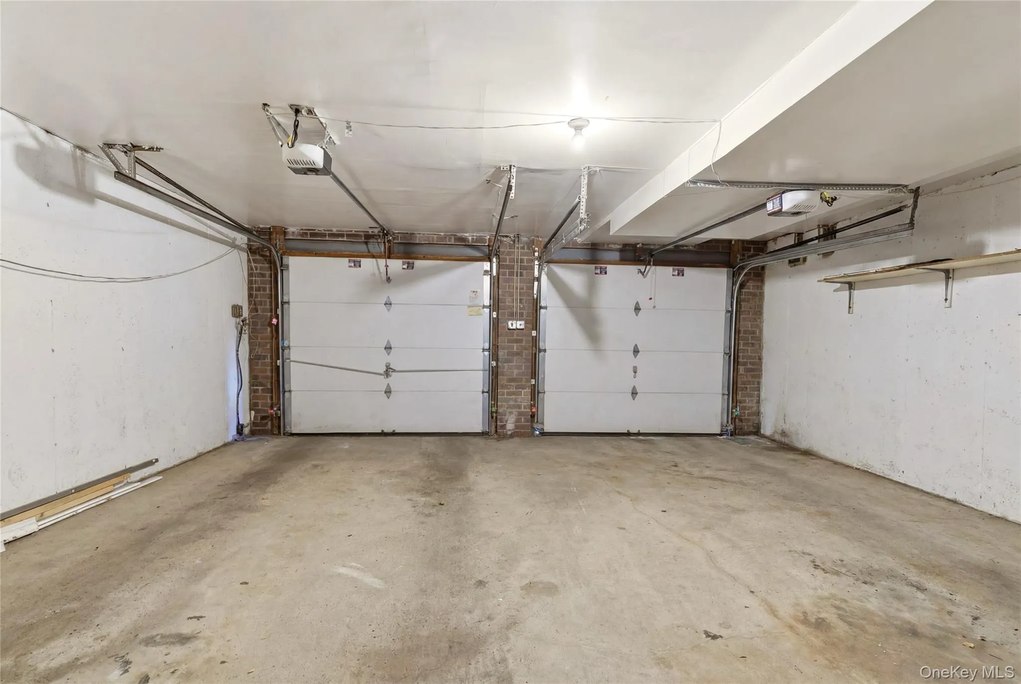 Two-car garage featuring concrete flooring, white overhead doors, and exposed brick accents Two-car garage featuring concrete flooring, white overhead doors, and exposed brick accents