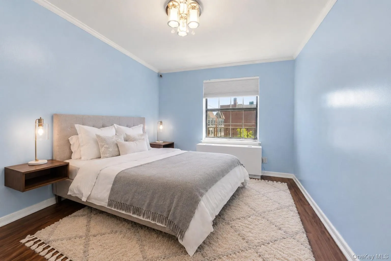 Light-filled room featuring hardwood flooring, crown molding, a window with a roller shade, and a built-in heating unit Light-filled room featuring hardwood flooring, crown molding, a window with a roller shade, and a built-in heating unit