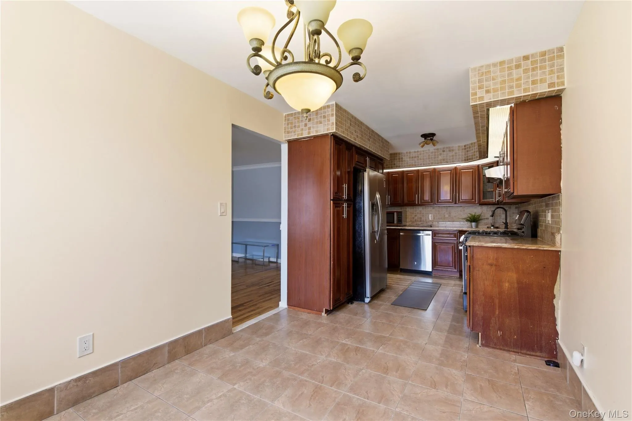 Kitchen featuring tile flooring, full-height tile backsplash, wood cabinetry, stainless steel appliances, and a granite-finish countertop Kitchen featuring tile flooring, full-height tile backsplash, wood cabinetry, stainless steel appliances, and a granite-finish countertop
