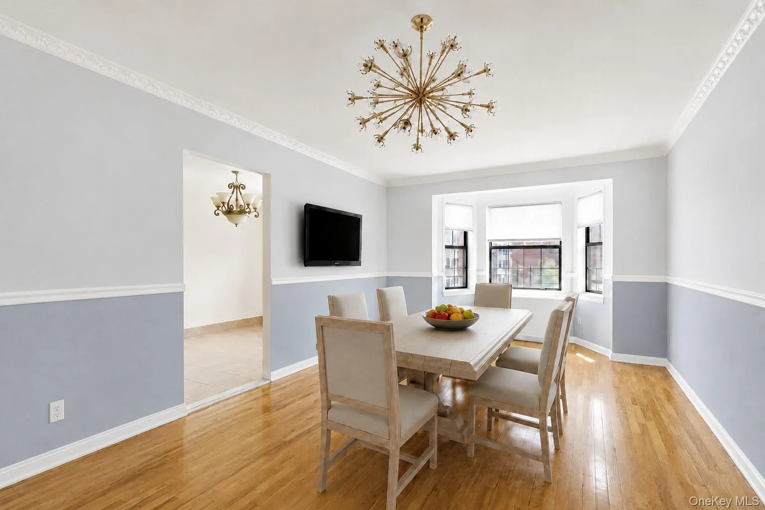 Dining area featuring wood-finish flooring, a contemporary sputnik-style chandelier, bay windows, two-tone painted walls with chair rail and crown molding Dining area featuring wood-finish flooring, a contemporary sputnik-style chandelier, bay windows, two-tone painted walls with chair rail and crown molding
