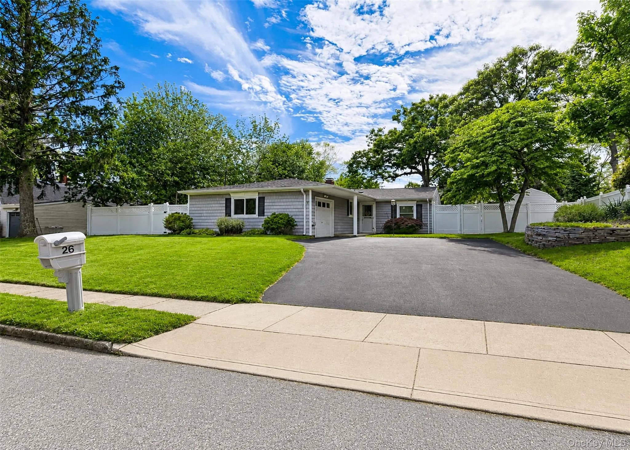 Ranch-style residence featuring grey siding, a black shingled roof, and a prominent asphalt driveway Ranch-style residence featuring grey siding, a black shingled roof, and a prominent asphalt driveway
