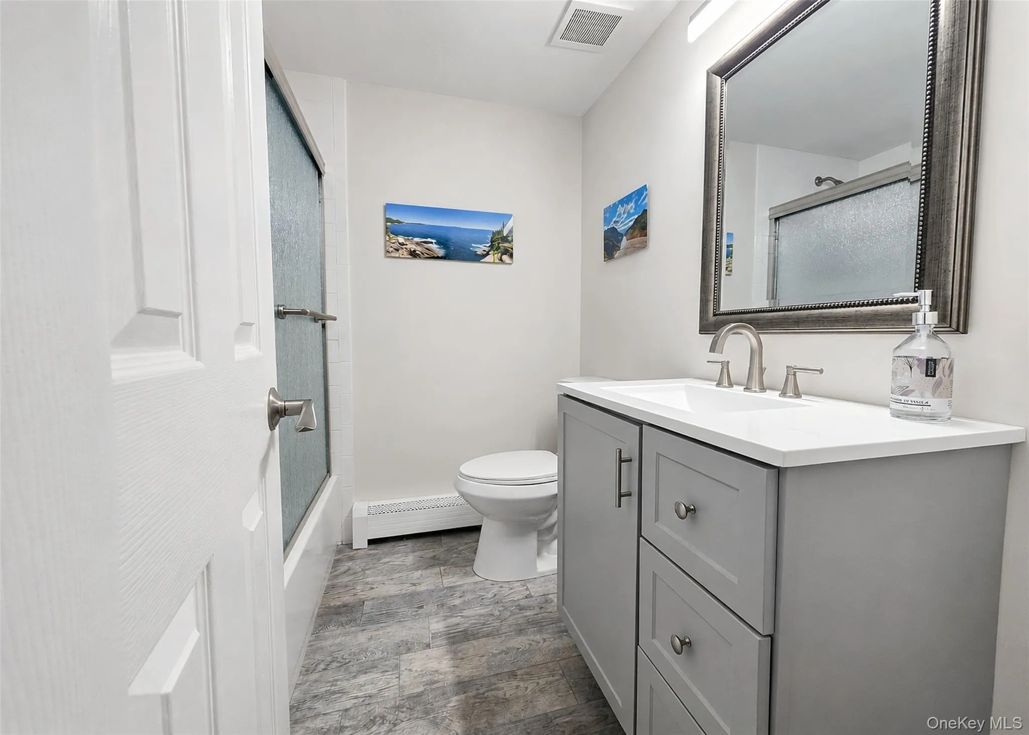 Bathroom featuring a contemporary gray vanity with a white countertop and rectangular sink, brushed nickel faucet, and a large framed mirror Bathroom featuring a contemporary gray vanity with a white countertop and rectangular sink, brushed nickel faucet, and a large framed mirror