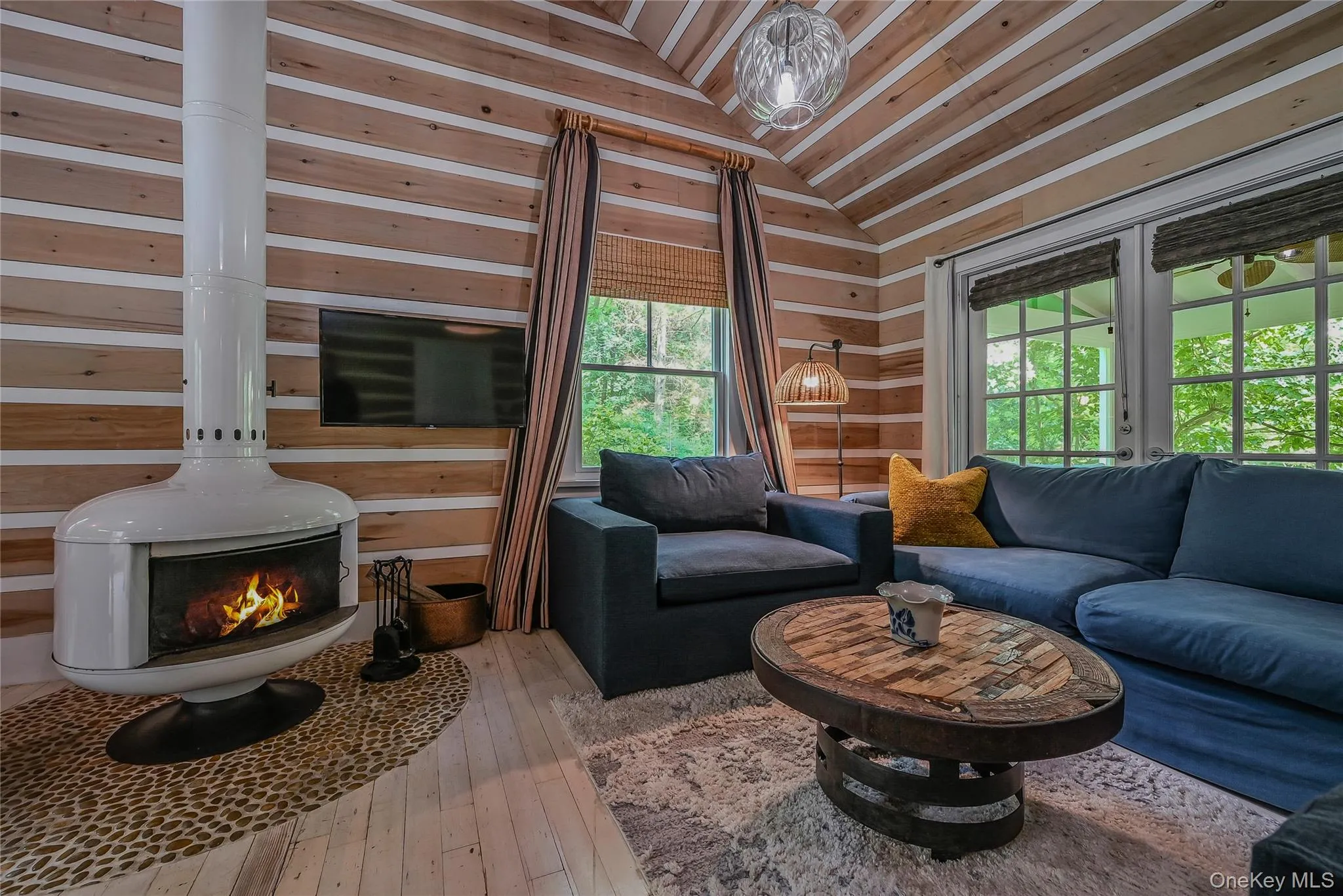 Living room featuring wood walls, vaulted ceiling, plenty of natural light, hardwood / wood-style flooring, and a wood stove Living room featuring wood walls, vaulted ceiling, plenty of natural light, hardwood / wood-style flooring, and a wood stove