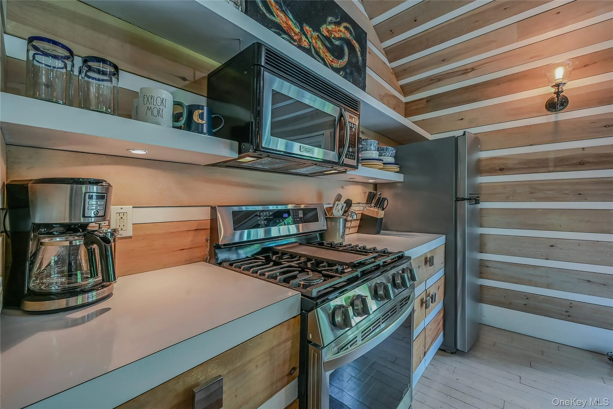 Kitchen featuring stainless steel appliances, light wood finished floors, and wooden walls Kitchen featuring stainless steel appliances, light wood finished floors, and wooden walls