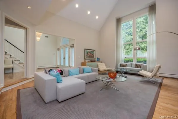 Vaulted ceiling living space featuring recessed lighting, a large window wall, wood-finish flooring, and a staircase with a white railing Vaulted ceiling living space featuring recessed lighting, a large window wall, wood-finish flooring, and a staircase with a white railing