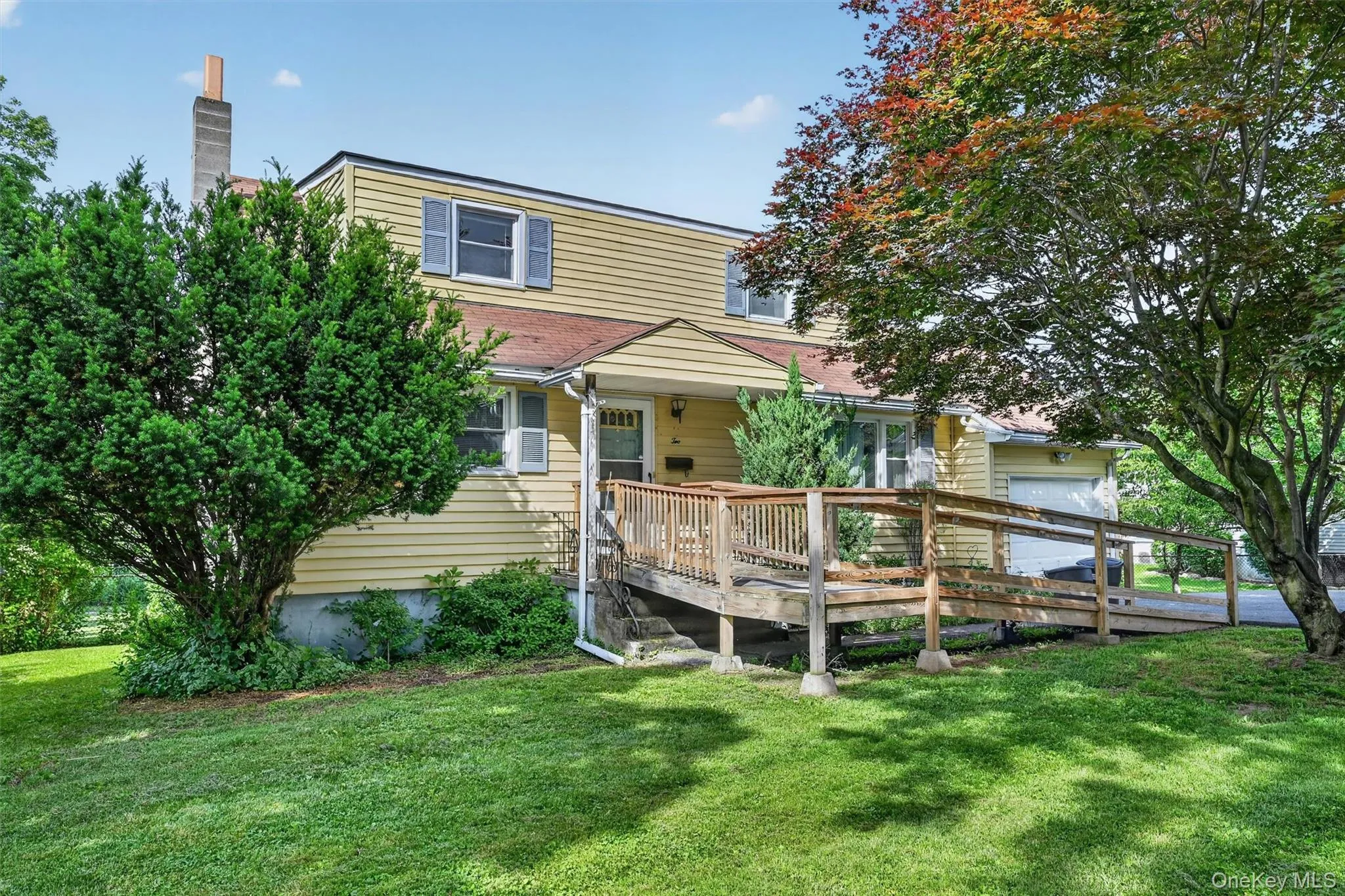 Two-story residence featuring light yellow siding, a wood ramp entry, and an integrated garage Two-story residence featuring light yellow siding, a wood ramp entry, and an integrated garage