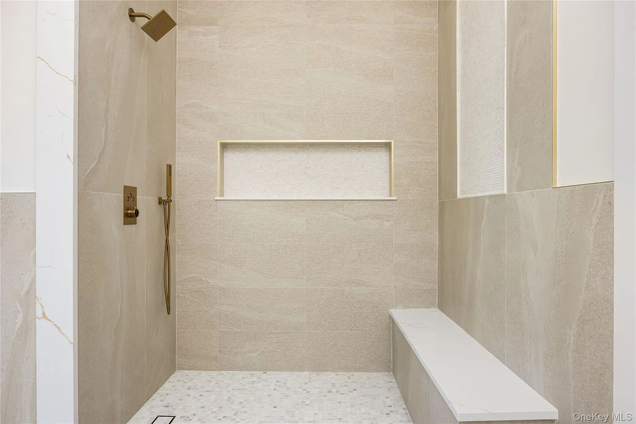 Walk-in shower with large format tile walls, mosaic tile flooring, built-in shower niche, and an integrated bench Walk-in shower with large format tile walls, mosaic tile flooring, built-in shower niche, and an integrated bench