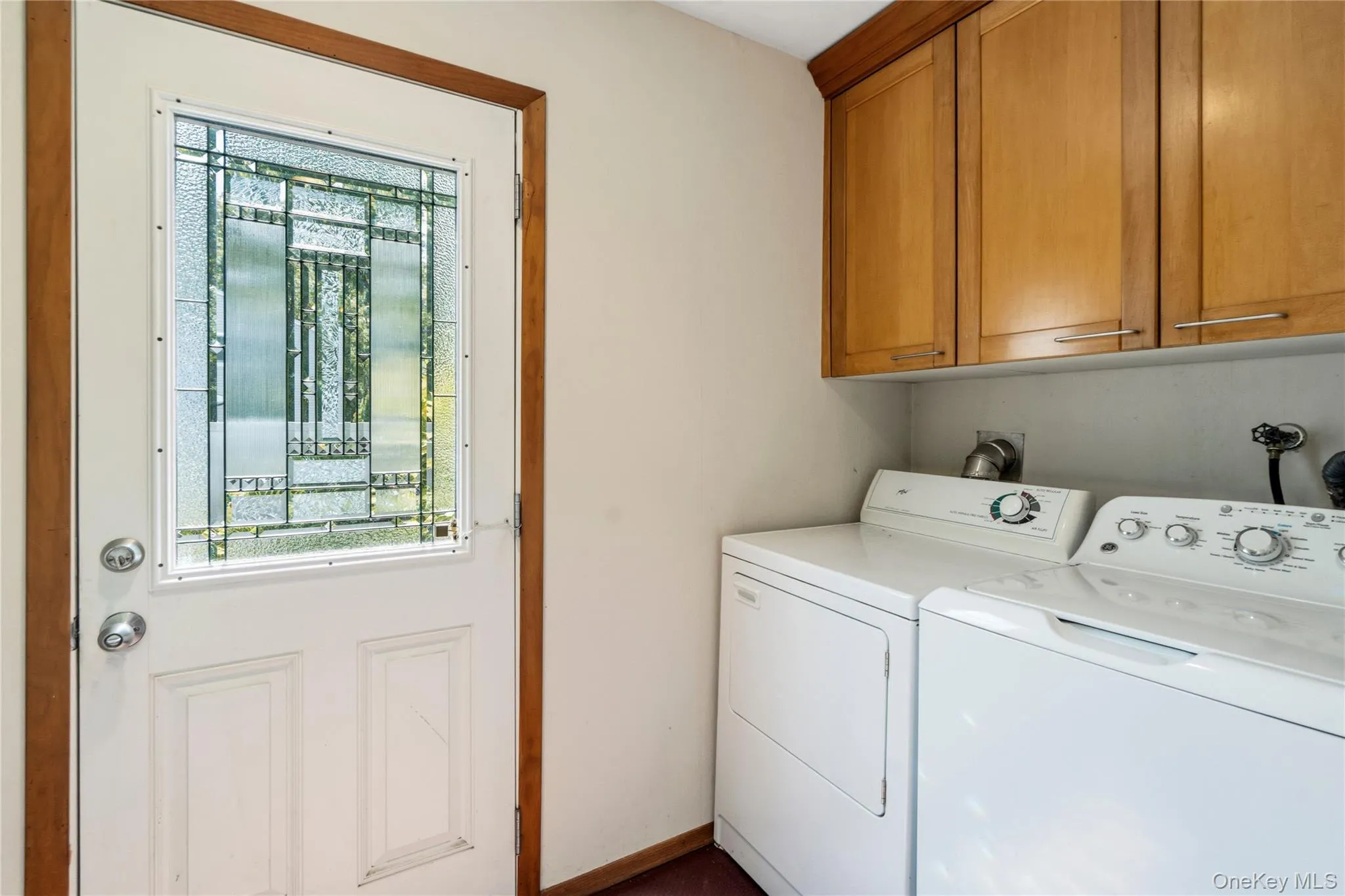Laundry area featuring a white paneled door with decorative glass, with both outdoor and garage access, wood-finish trim, upper cabinetry, and dedicated appliance space Laundry area featuring a white paneled door with decorative glass, with both outdoor and garage access, wood-finish trim, upper cabinetry, and dedicated appliance space