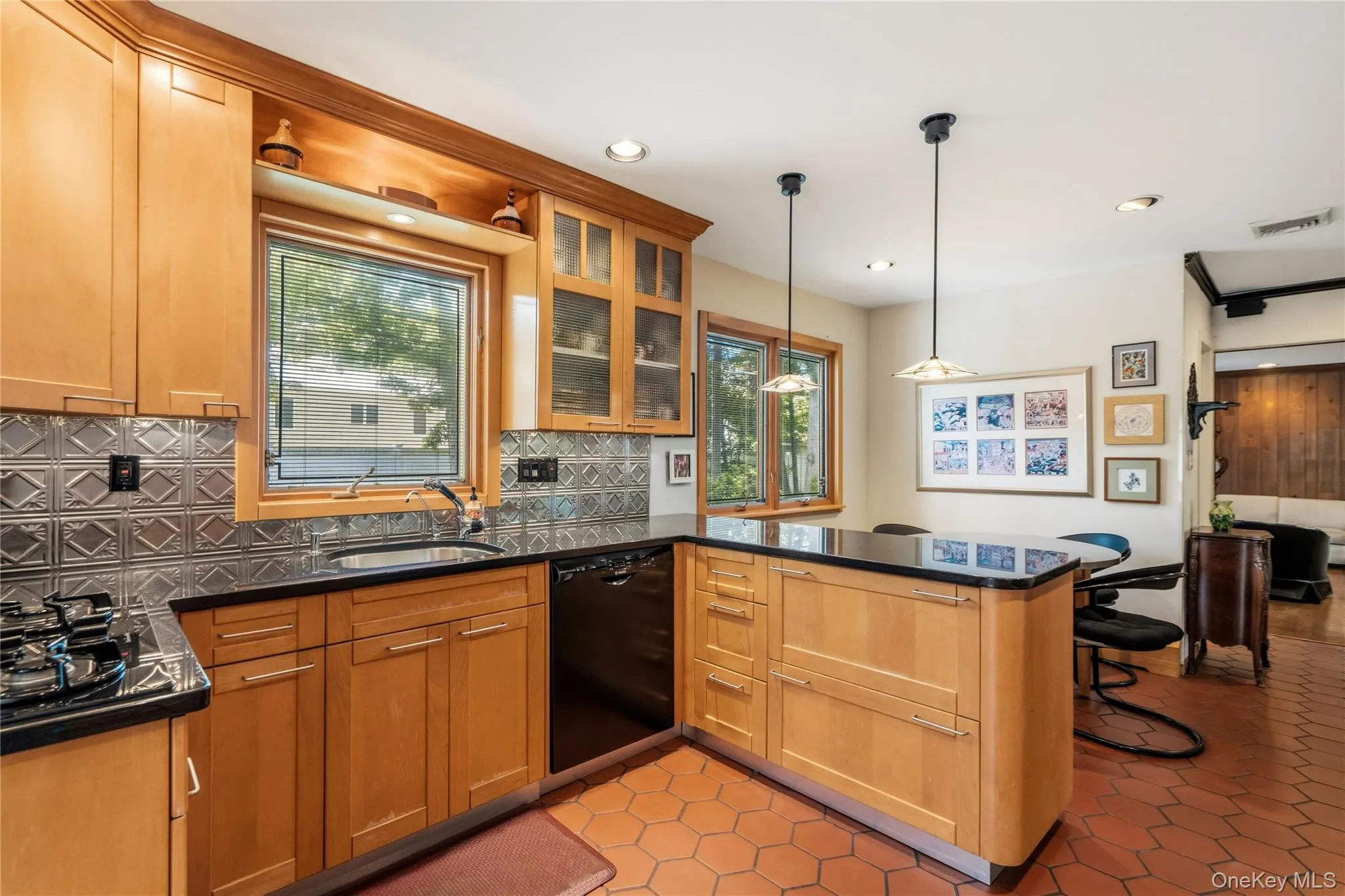 Kitchen featuring light wood cabinetry, black granite countertops, tile flooring, a pressed tin-style backsplash, and recessed and pendant lighting Kitchen featuring light wood cabinetry, black granite countertops, tile flooring, a pressed tin-style backsplash, and recessed and pendant lighting
