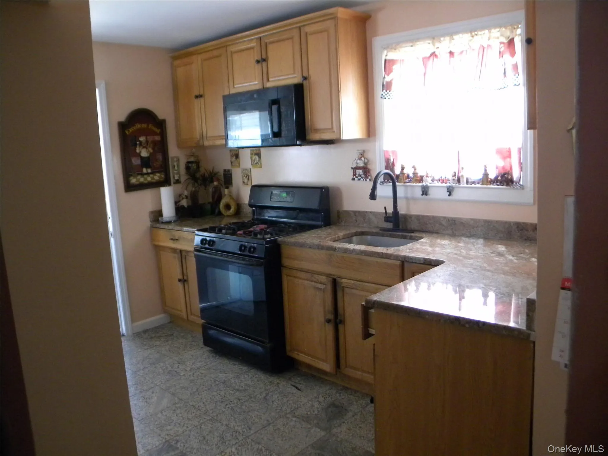 Kitchen featuring wood-finish cabinetry, black appliances including an oven range and microwave, granite-style countertops, and a single basin sink with a dark-finish faucet Kitchen featuring wood-finish cabinetry, black appliances including an oven range and microwave, granite-style countertops, and a single basin sink with a dark-finish faucet