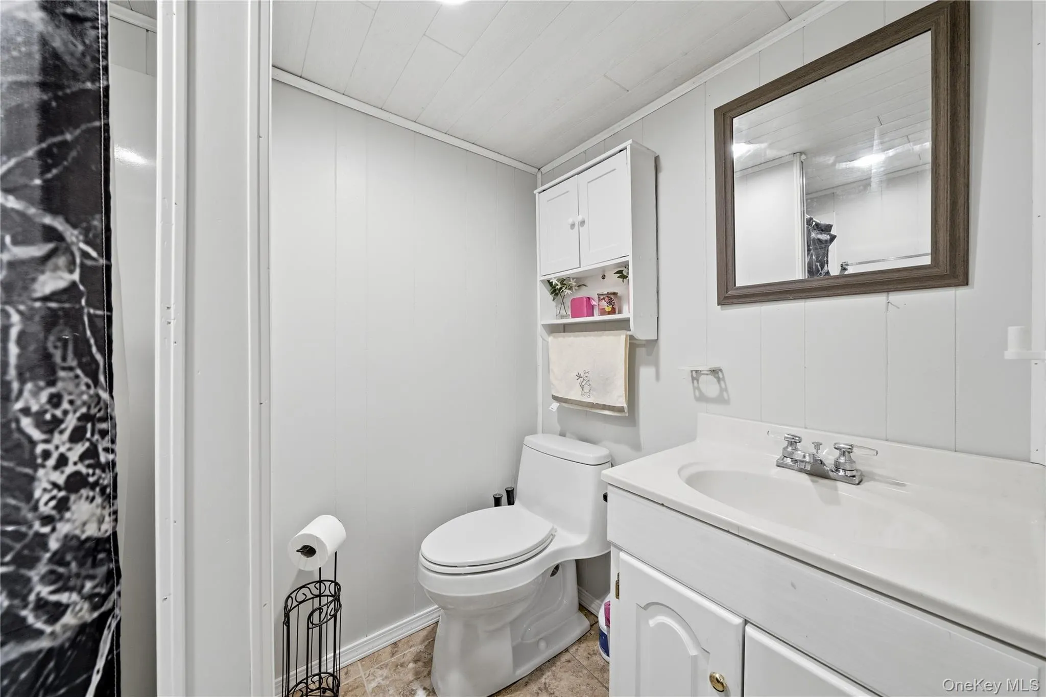 Bathroom featuring a white vanity with integrated sink, framed wall mirror, white paneled walls, and a white ceiling with recessed lighting Bathroom featuring a white vanity with integrated sink, framed wall mirror, white paneled walls, and a white ceiling with recessed lighting