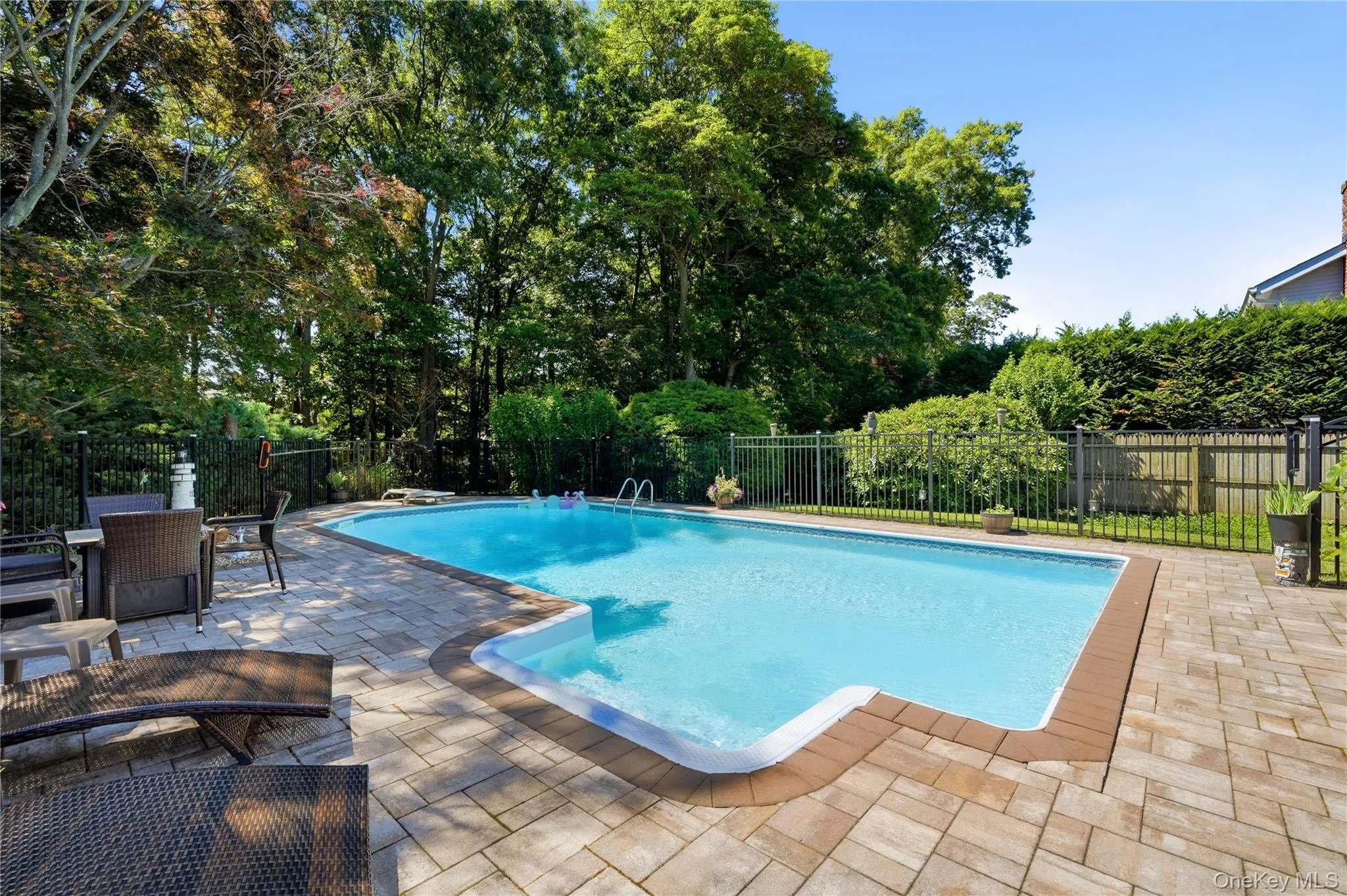 Rectangular swimming pool surrounded by a paver patio and mature trees, featuring a black metal fence Rectangular swimming pool surrounded by a paver patio and mature trees, featuring a black metal fence