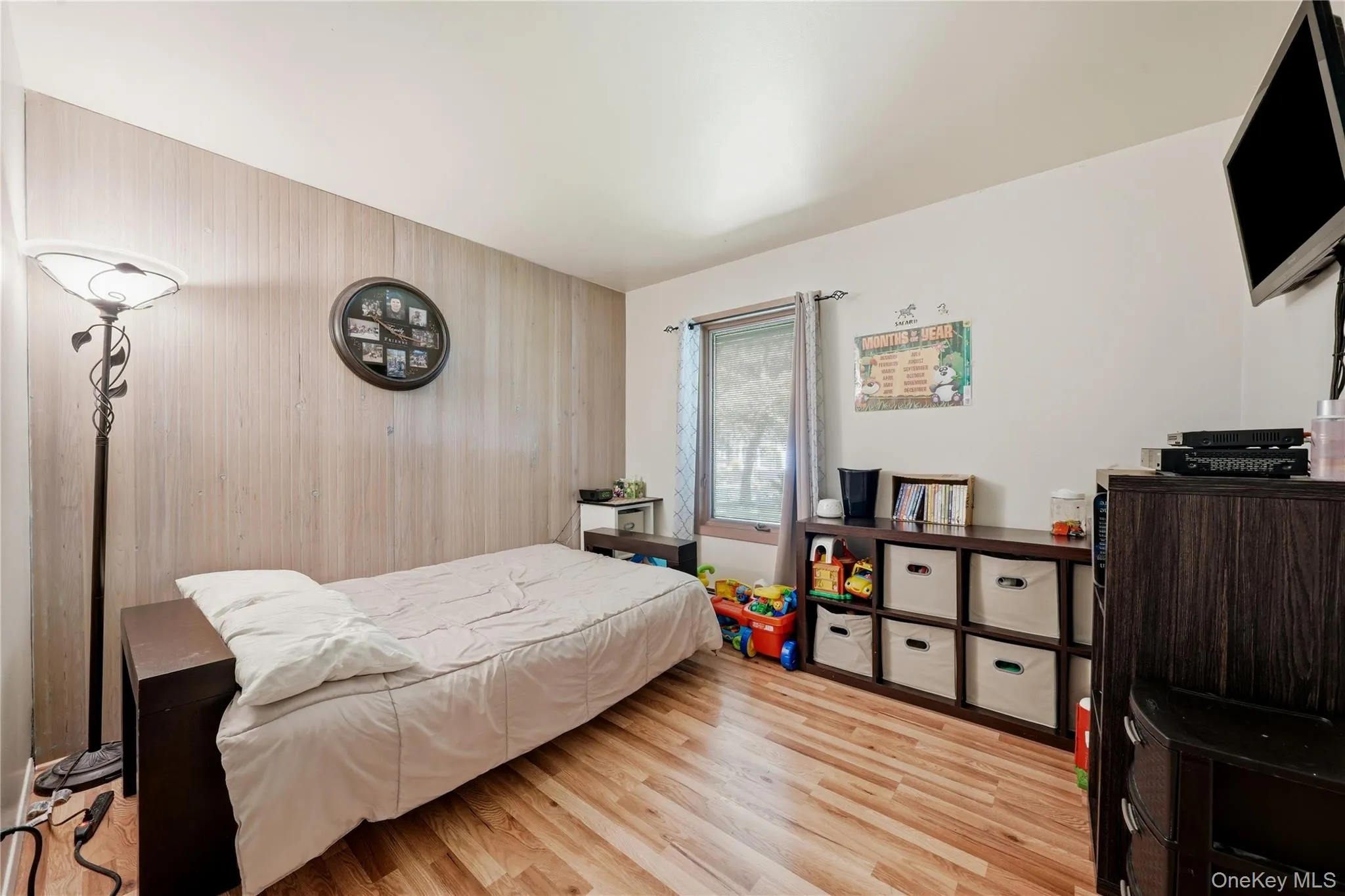 Room featuring wood-finish flooring, a neutral wall color, and a window with curtains Room featuring wood-finish flooring, a neutral wall color, and a window with curtains