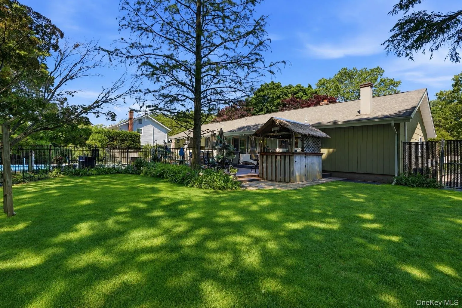 Expansive manicured lawn with mature trees, a fenced inground pool, and a private patio with an outdoor bar structure Expansive manicured lawn with mature trees, a fenced inground pool, and a private patio with an outdoor bar structure