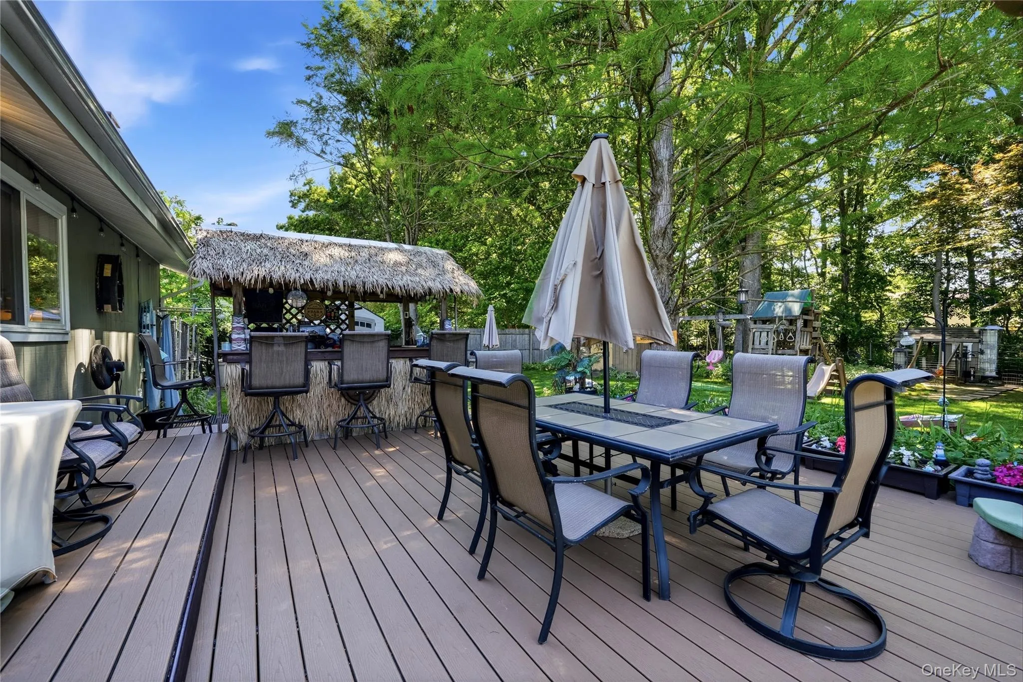 Spacious composite deck featuring a built-in outdoor bar with a thatched roof and a dining area with a tile-top table Spacious composite deck featuring a built-in outdoor bar with a thatched roof and a dining area with a tile-top table