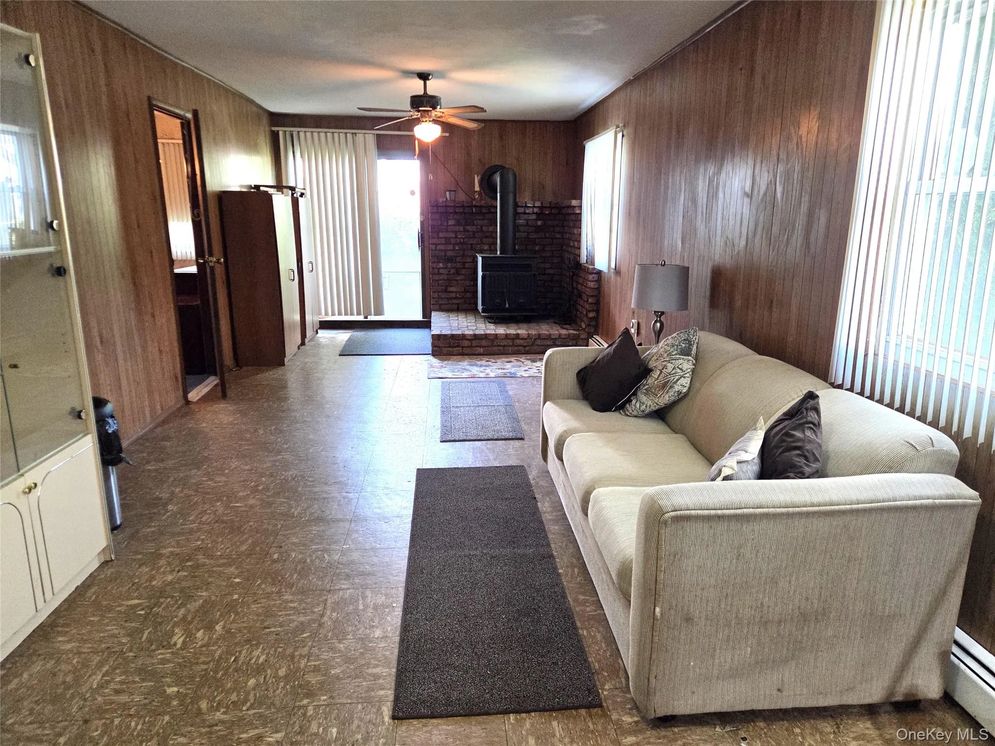 The Large Lower Level Living Room/Den Offers Two Outside Entrances - A Side Door & Back Sliding Doors, Two Large Windows For Natural Light, Wood Burning Stove With Brick Surround, Ceiling Fan, And Ample Room For Furniture. The Large Lower Level Living Room/Den Offers Two Outside Entrances - A Side Door & Back Sliding Doors, Two Large Windows For Natural Light, Wood Burning Stove With Brick Surround, Ceiling Fan, And Ample Room For Furniture.
