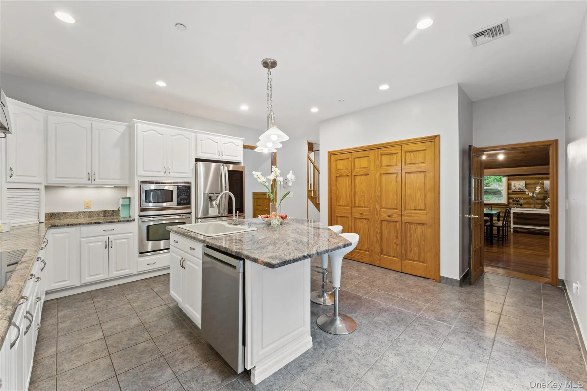Well-appointed kitchen featuring a central island with an integrated sink and breakfast bar, white cabinetry, stainless steel appliances, recessed lighting, and tiled flooring Well-appointed kitchen featuring a central island with an integrated sink and breakfast bar, white cabinetry, stainless steel appliances, recessed lighting, and tiled flooring