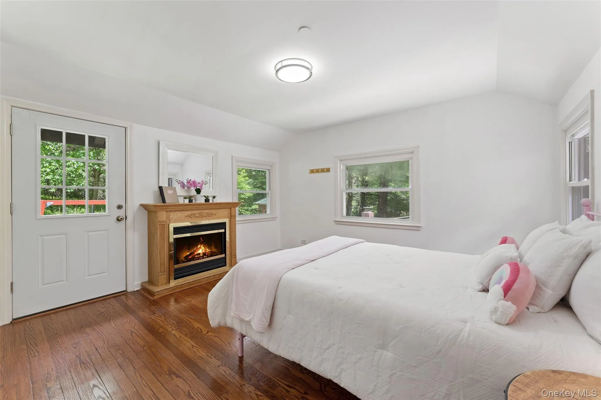 First floor bedroom featuring rich wood-finish flooring, a light wood-finish fireplace, and multiple windows First floor bedroom featuring rich wood-finish flooring, a light wood-finish fireplace, and multiple windows
