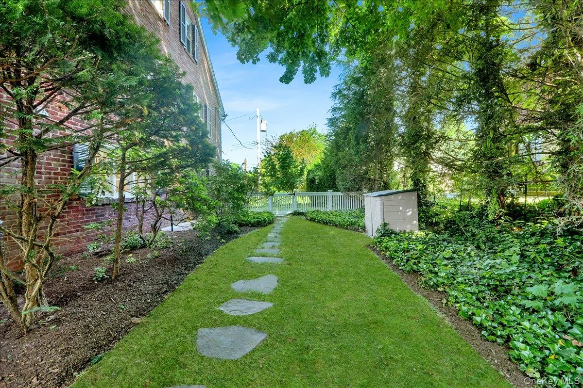 Manicured lawn pathway with stepping stones, bordered by a privacy fence, mature trees, and an accessory storage shed Manicured lawn pathway with stepping stones, bordered by a privacy fence, mature trees, and an accessory storage shed