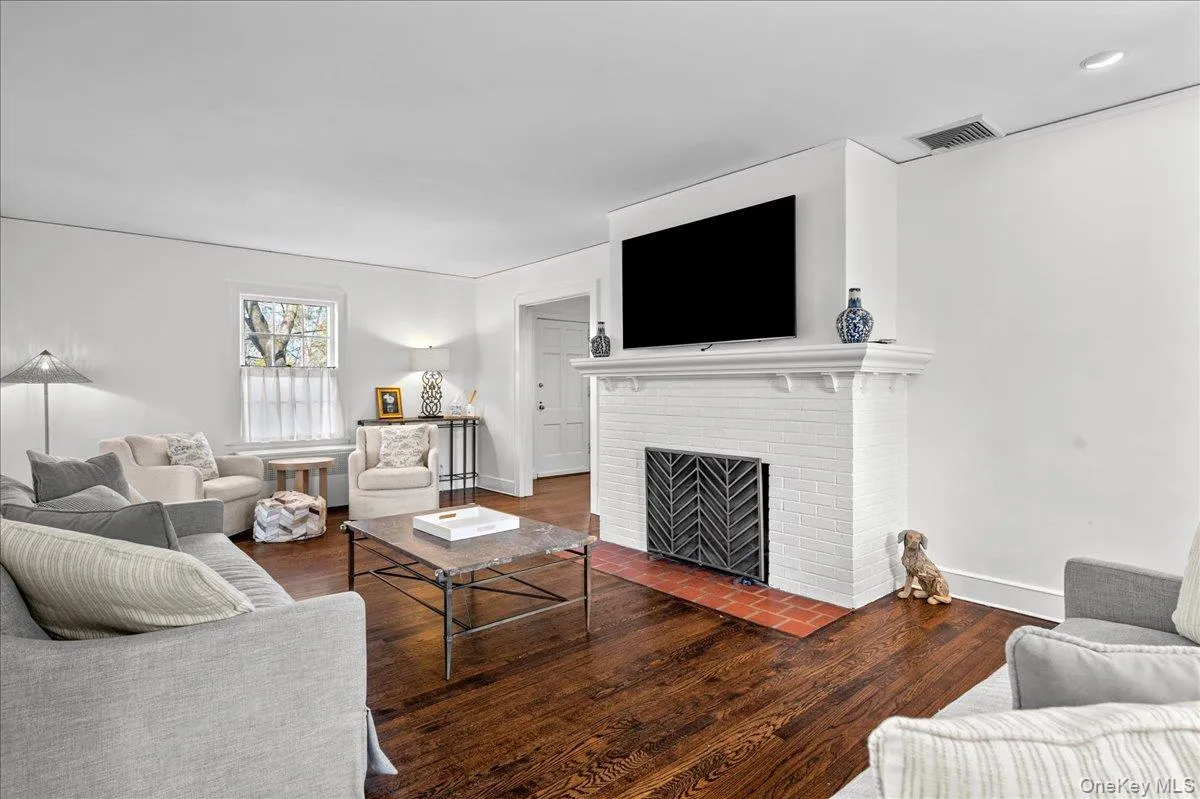 Living room featuring rich wood-finish flooring and a white brick fireplace with a decorative screen Living room featuring rich wood-finish flooring and a white brick fireplace with a decorative screen