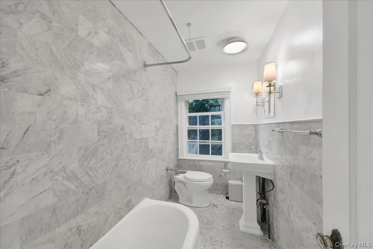 2nd floor bathroom featuring full-height marble-look wall tiling, a pedestal sink, and a porcelain toilet 2nd floor bathroom featuring full-height marble-look wall tiling, a pedestal sink, and a porcelain toilet