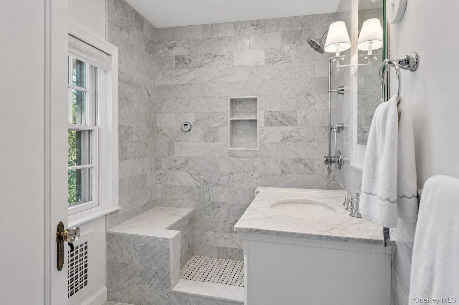 En suite primary bathroom featuring a walk-in shower with integrated bench and niche, white subway tile walls, and a white vanity with an undermount sink En suite primary bathroom featuring a walk-in shower with integrated bench and niche, white subway tile walls, and a white vanity with an undermount sink